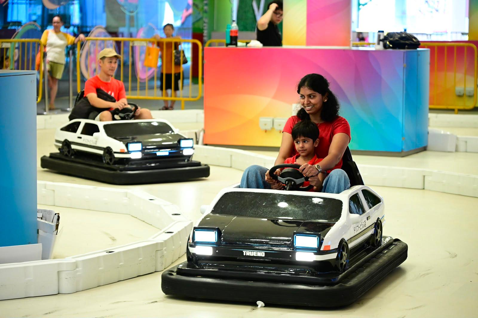Woman and child riding an AE86-Trueno-styled bumper car at an indoor attraction
