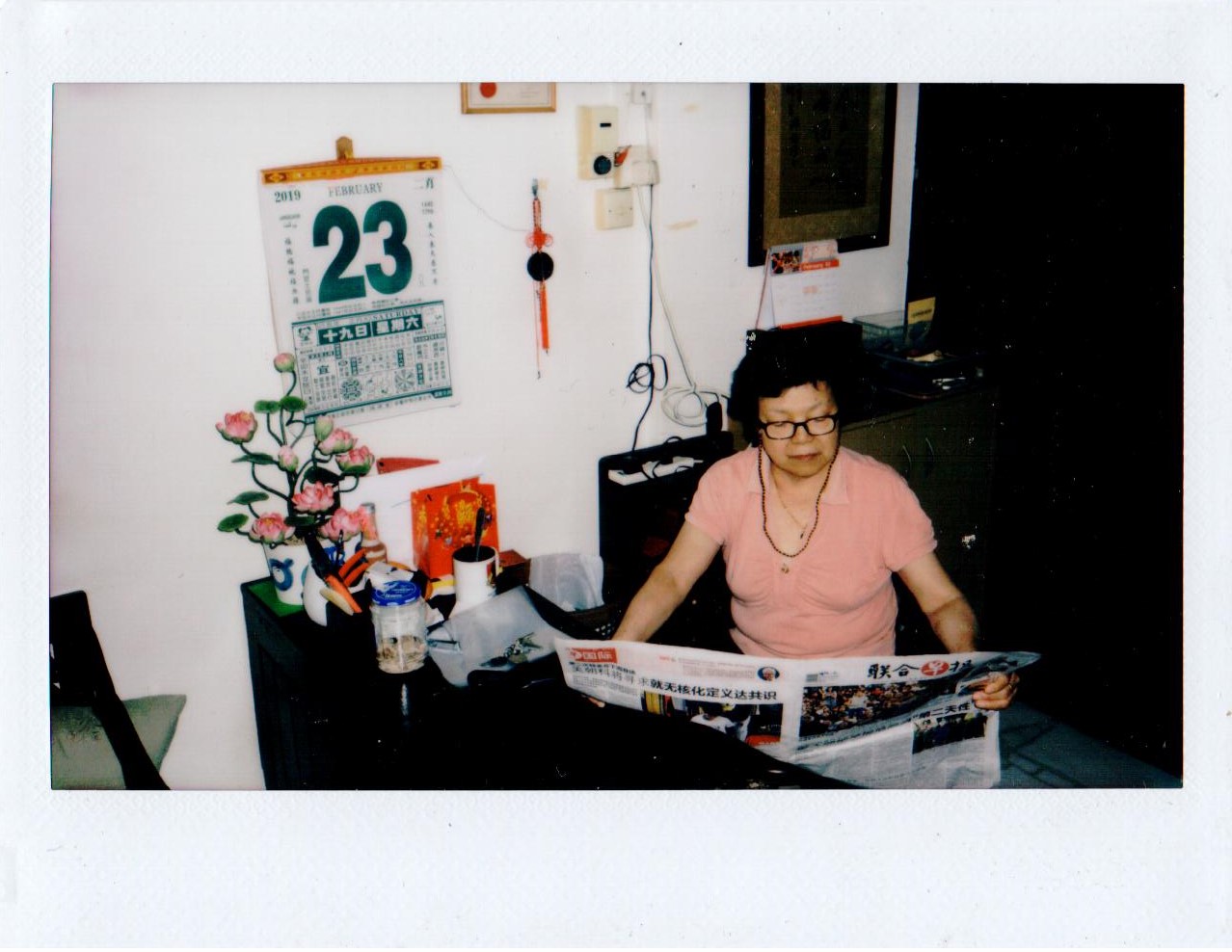 A woman sitting reading a newspaper in a room with a calendar