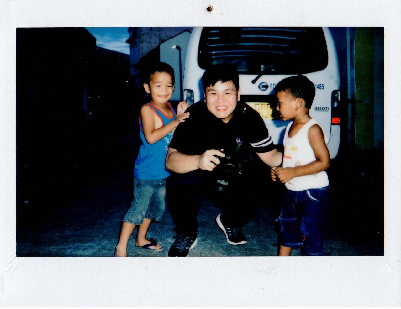 A photographer crouching beside two children in front of a white van