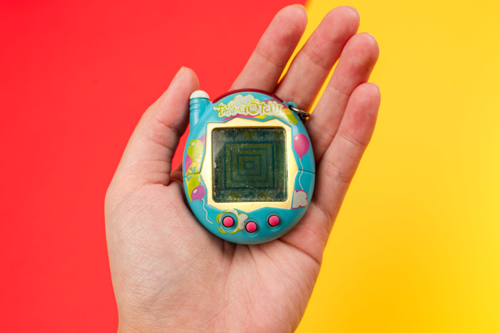 A hand holding a teal Tamagotchi