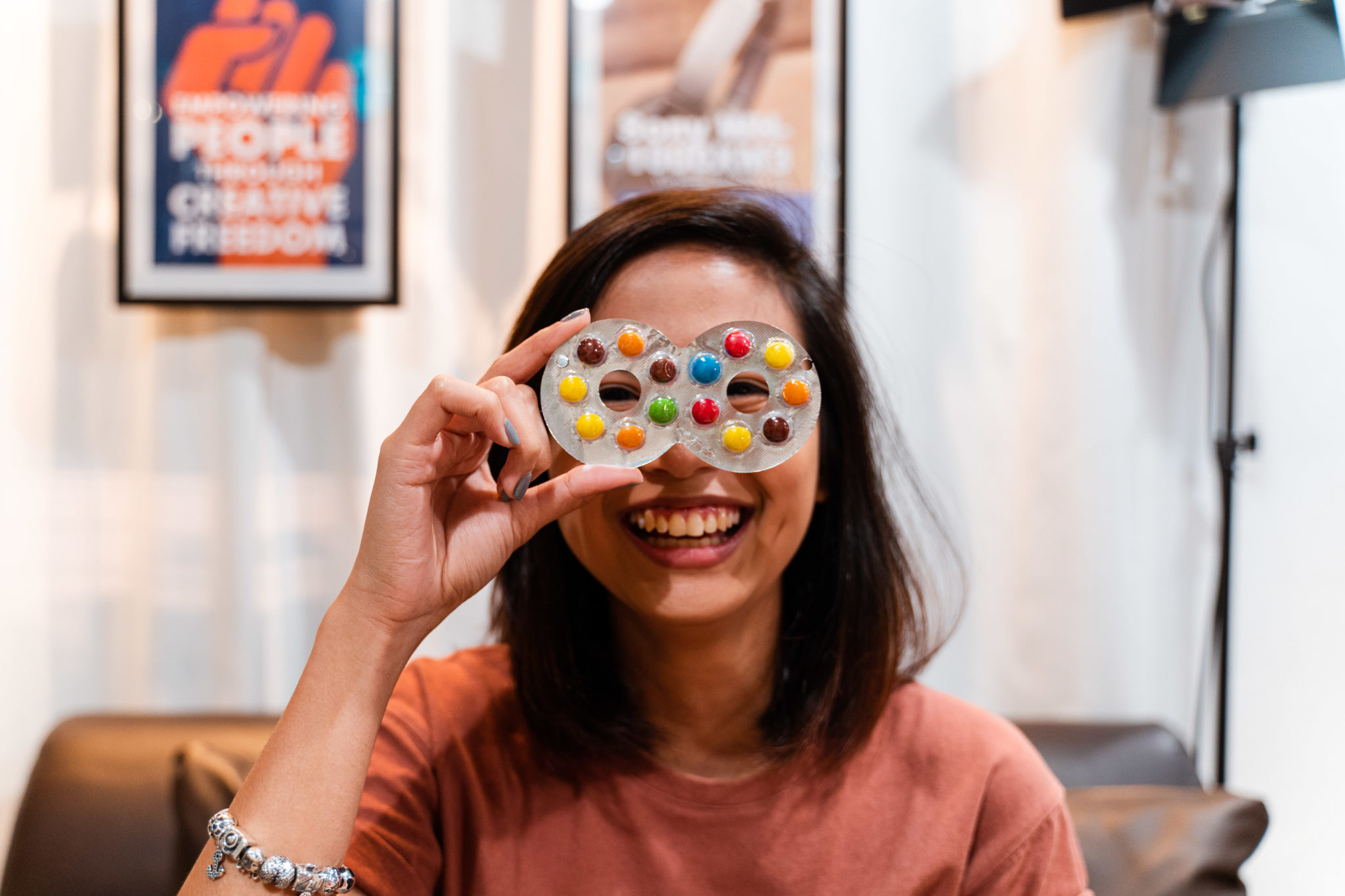 A smiling woman holding an iced gem biscuit in front of her eyes