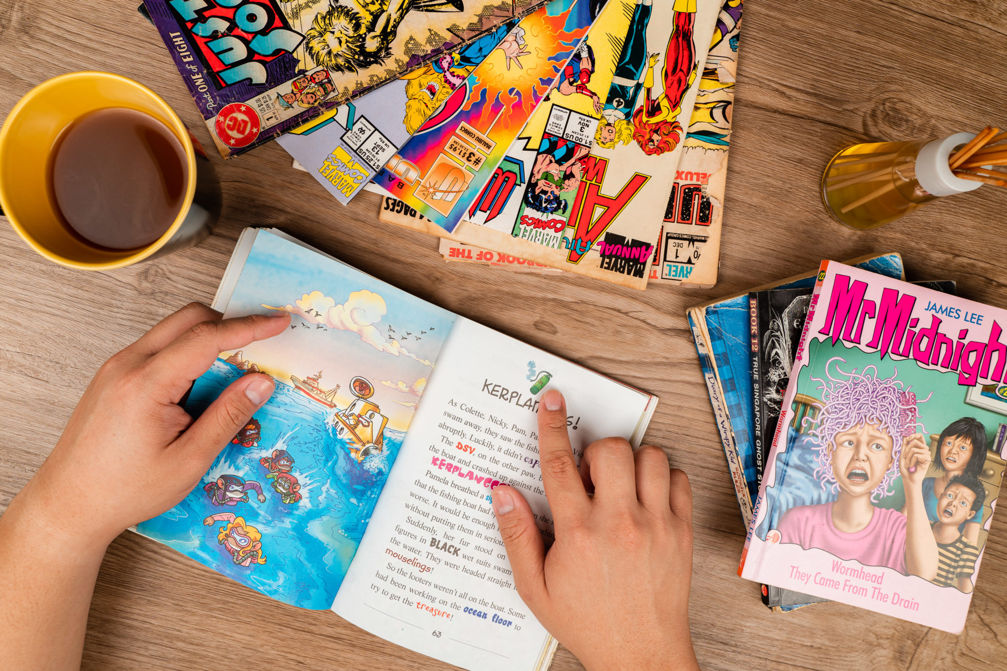 Hands turning the pages of a colourfully illustrated children's book beside comics