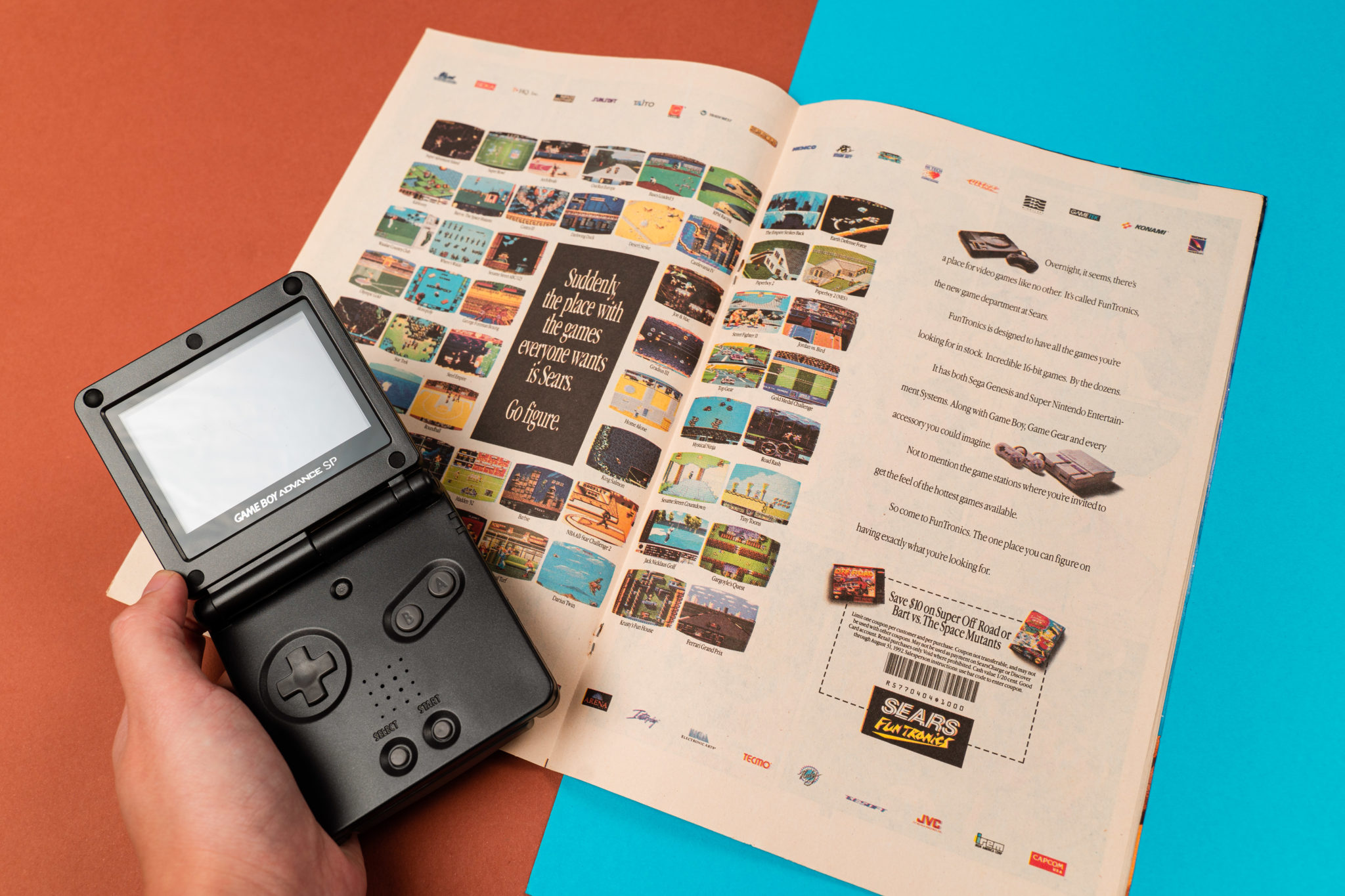 A hand holding a Game Boy Advance SP over a page of game advertisements
