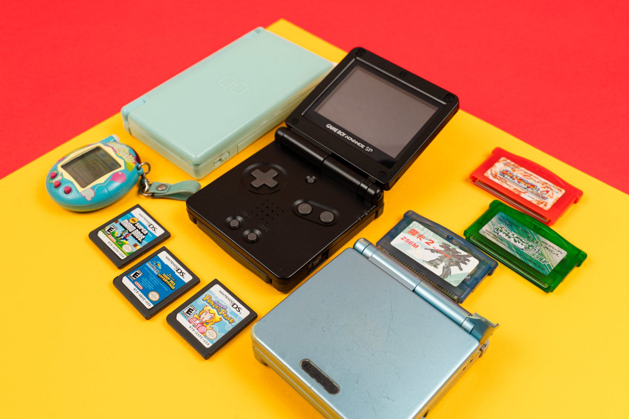 Game Boy Advance consoles, a Tamagotchi and game cartridges laid out together