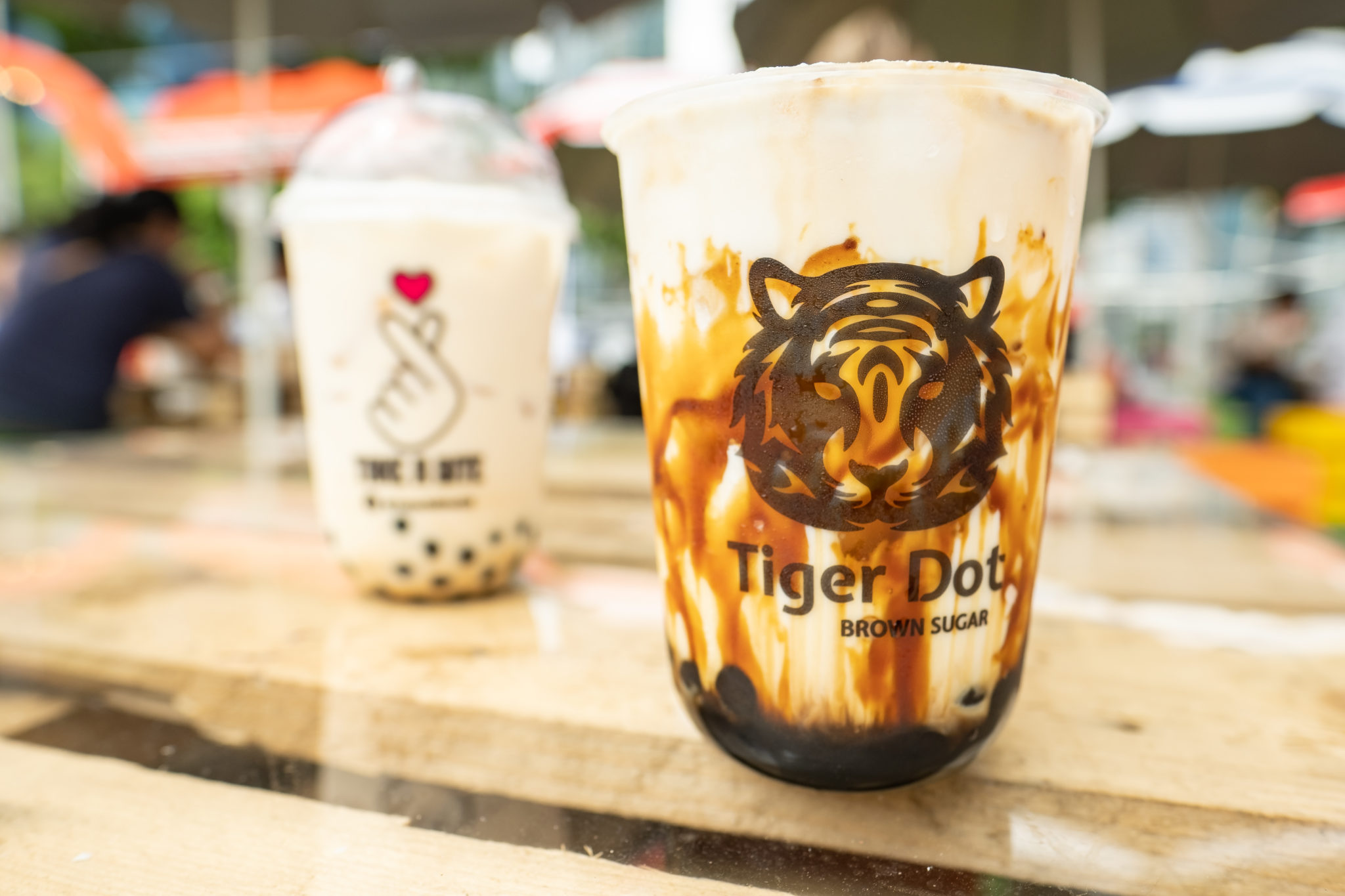 Two bobba tea cups on a wooden table, one with a tiger design