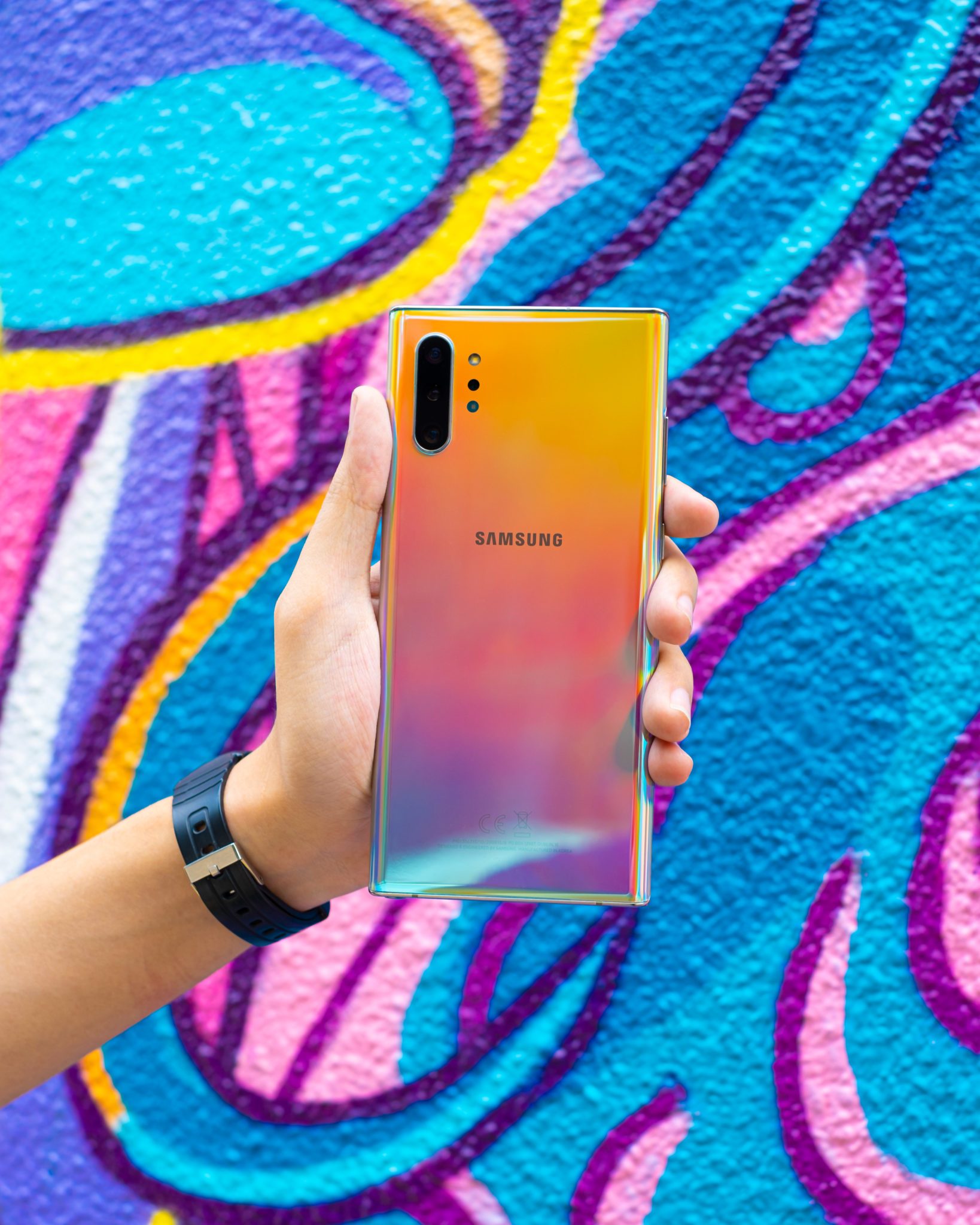 The Note 10+ held in one hand against a colourful mural, showing its back and camera