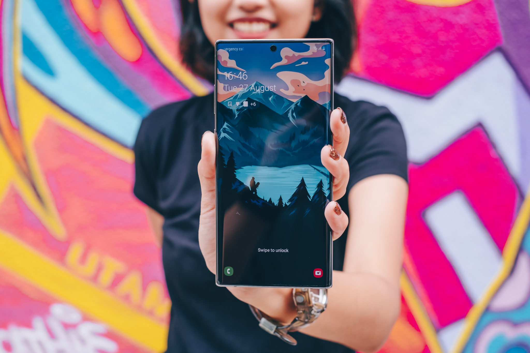 A woman in front of a colourful mural holding up the Note 10+ with its display on