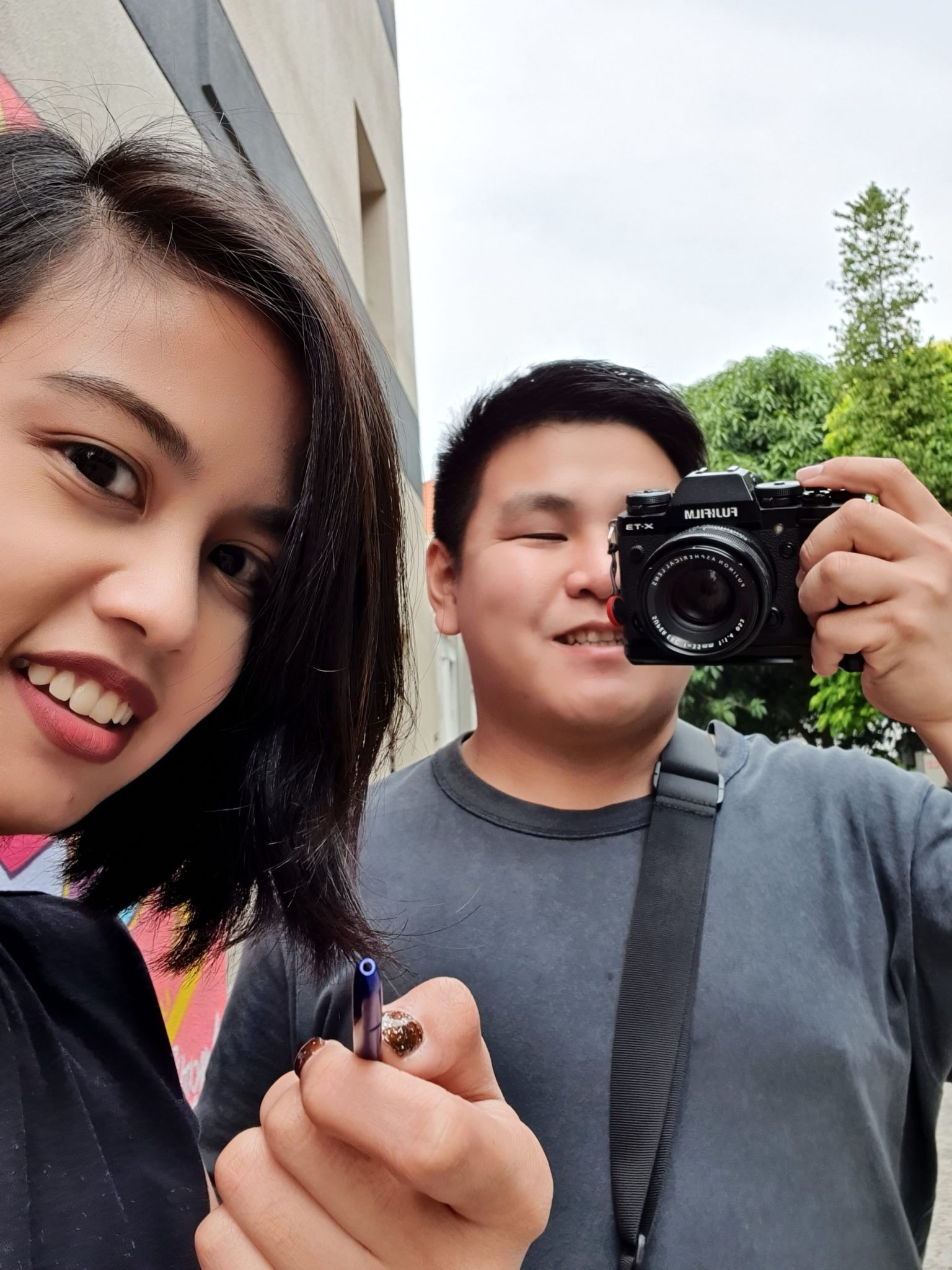 A woman holding the S Pen beside a man with a camera, both smiling