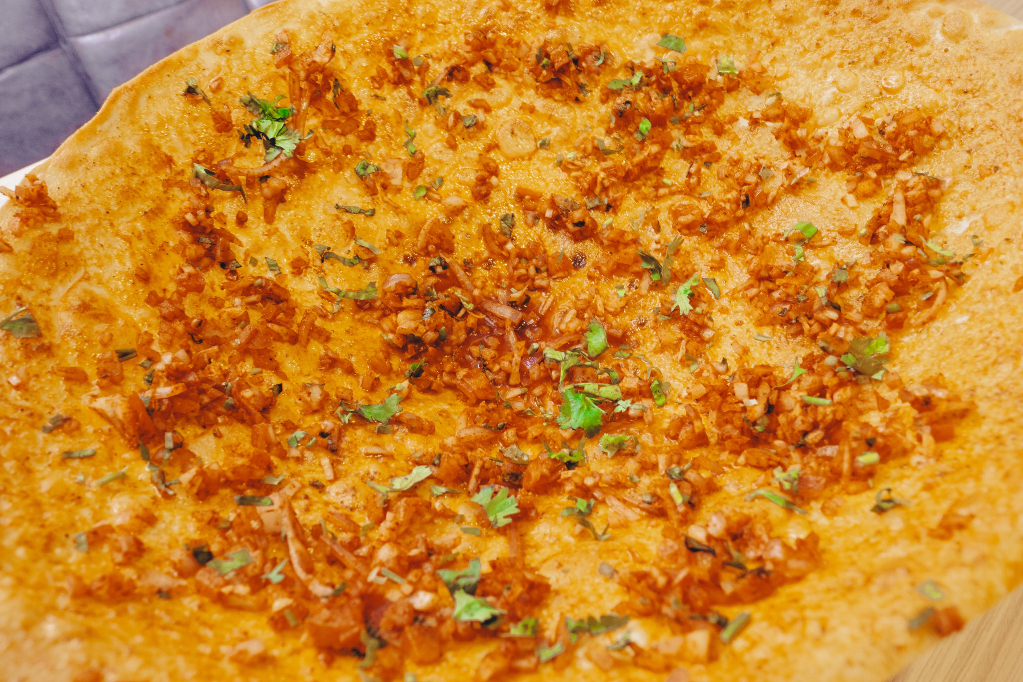 A large thin flatbread topped with diced onions and herbs