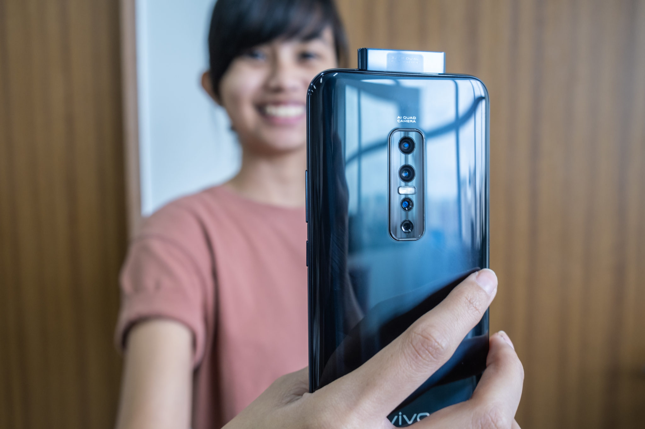 A woman smiling behind a Vivo V17 Pro held with its pop-up camera raised