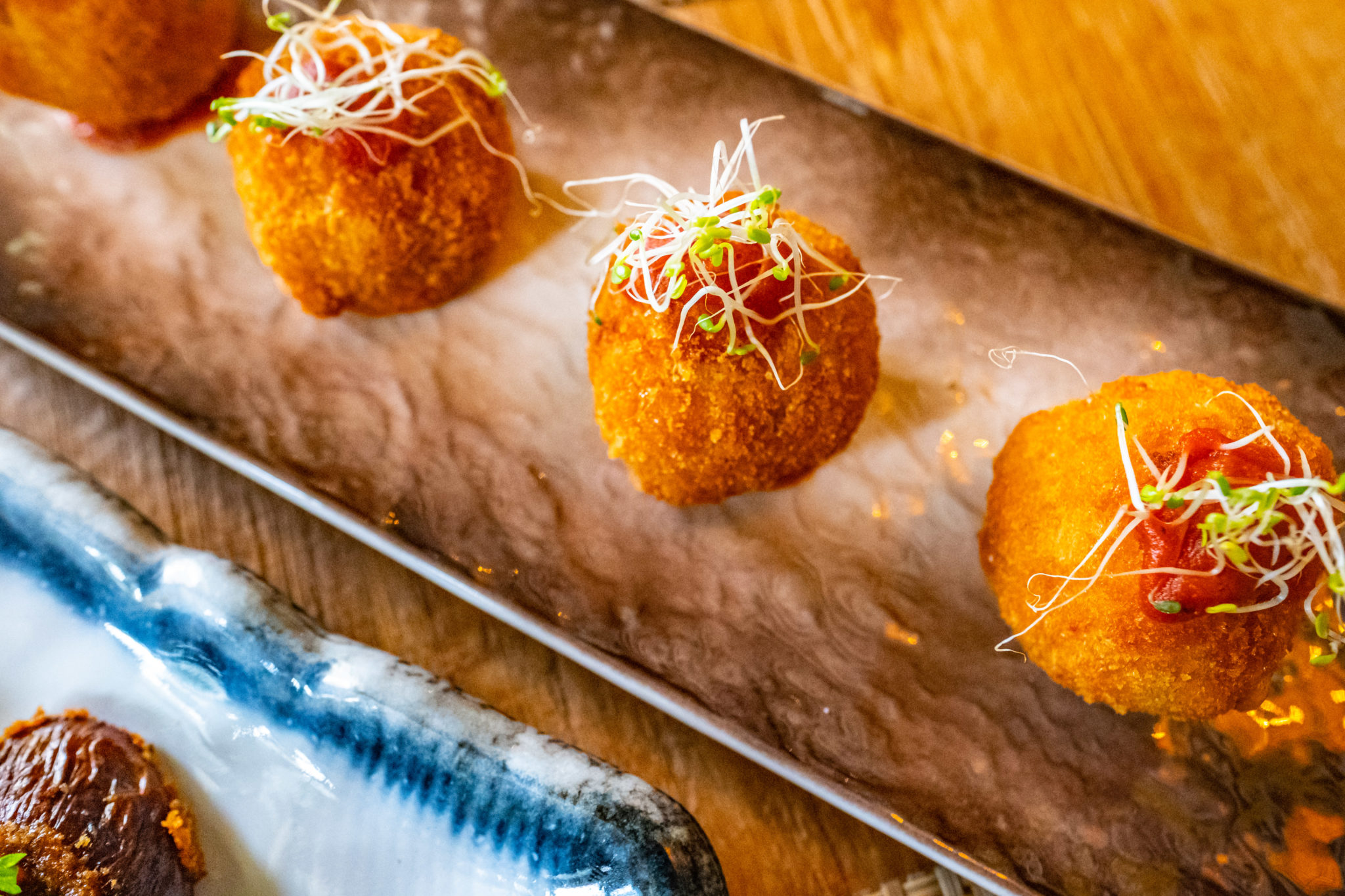 Golden fried Mac Balls topped with shredded greens on a long plate