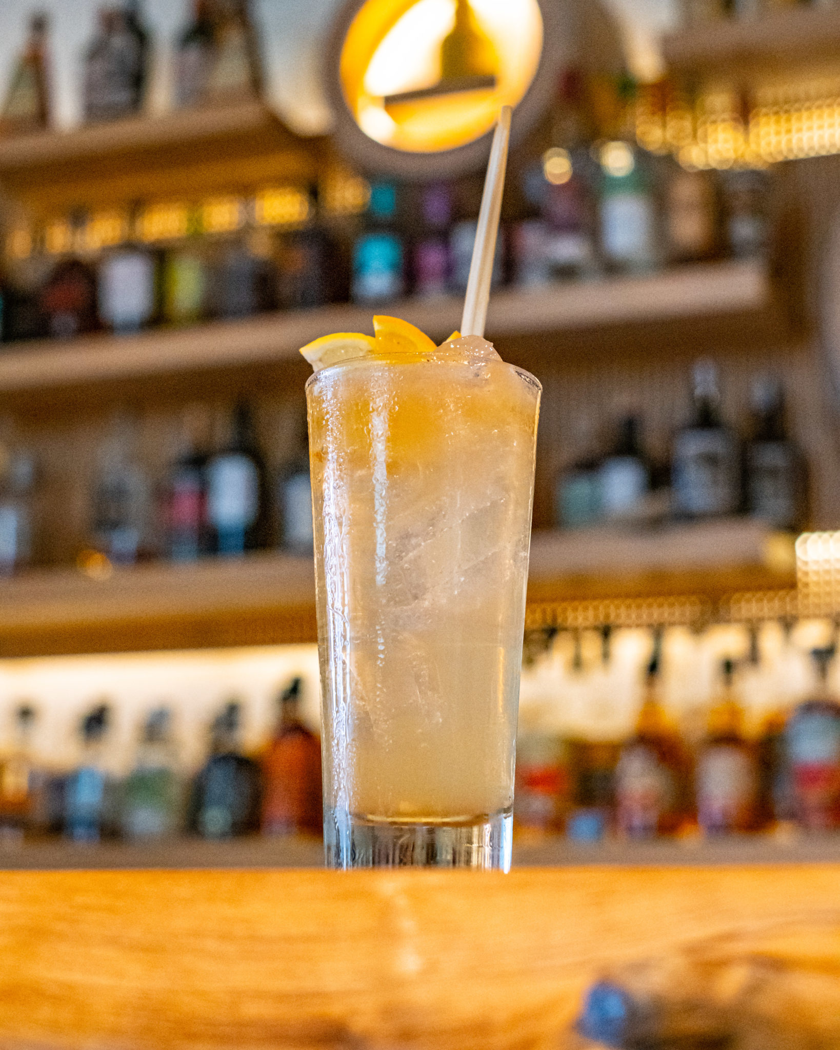 A tall Kingston Duo cocktail in front of the bar shelves