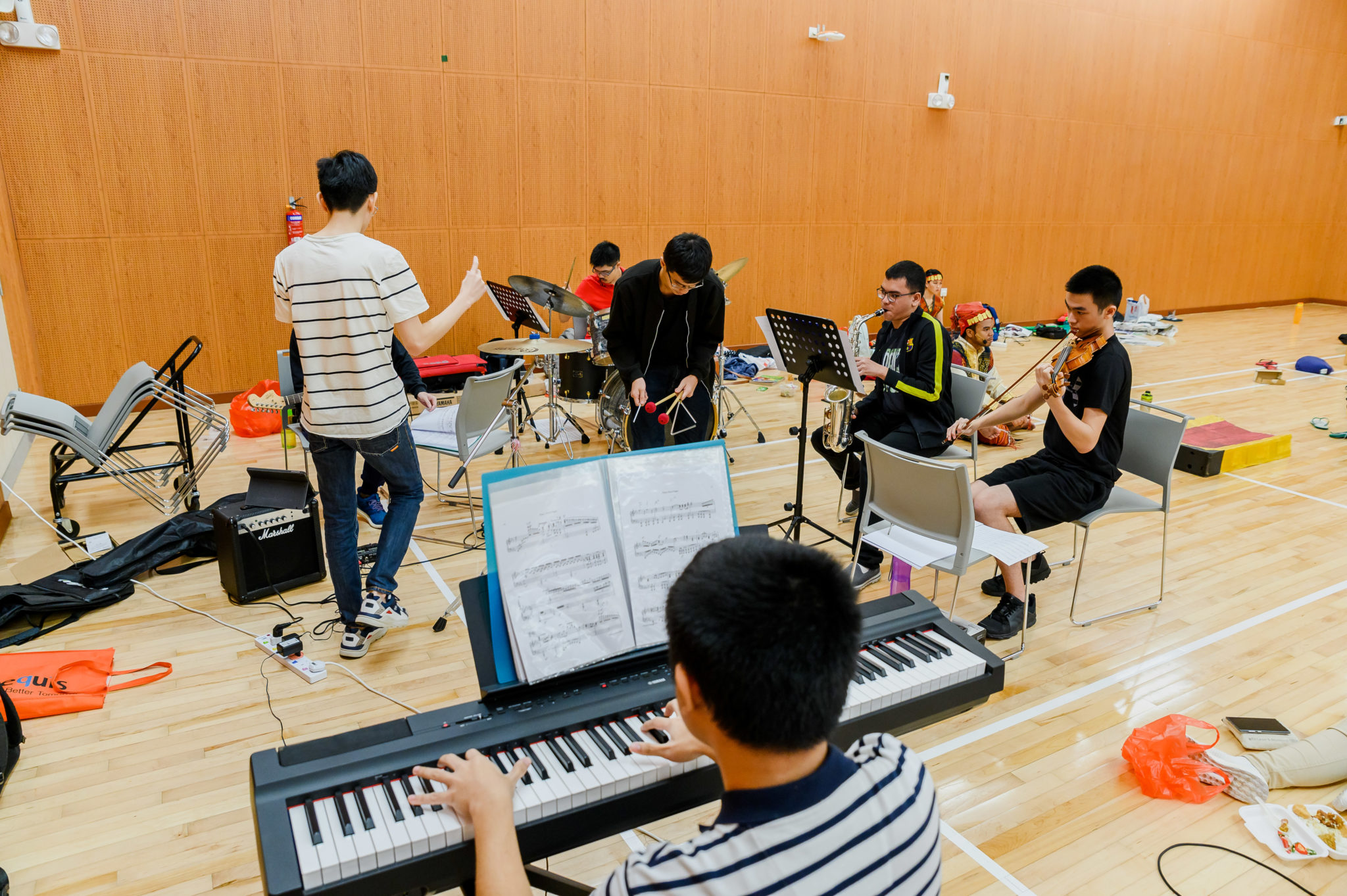 Musicians and a conductor rehearsing the score at a keyboard in the rehearsal hall