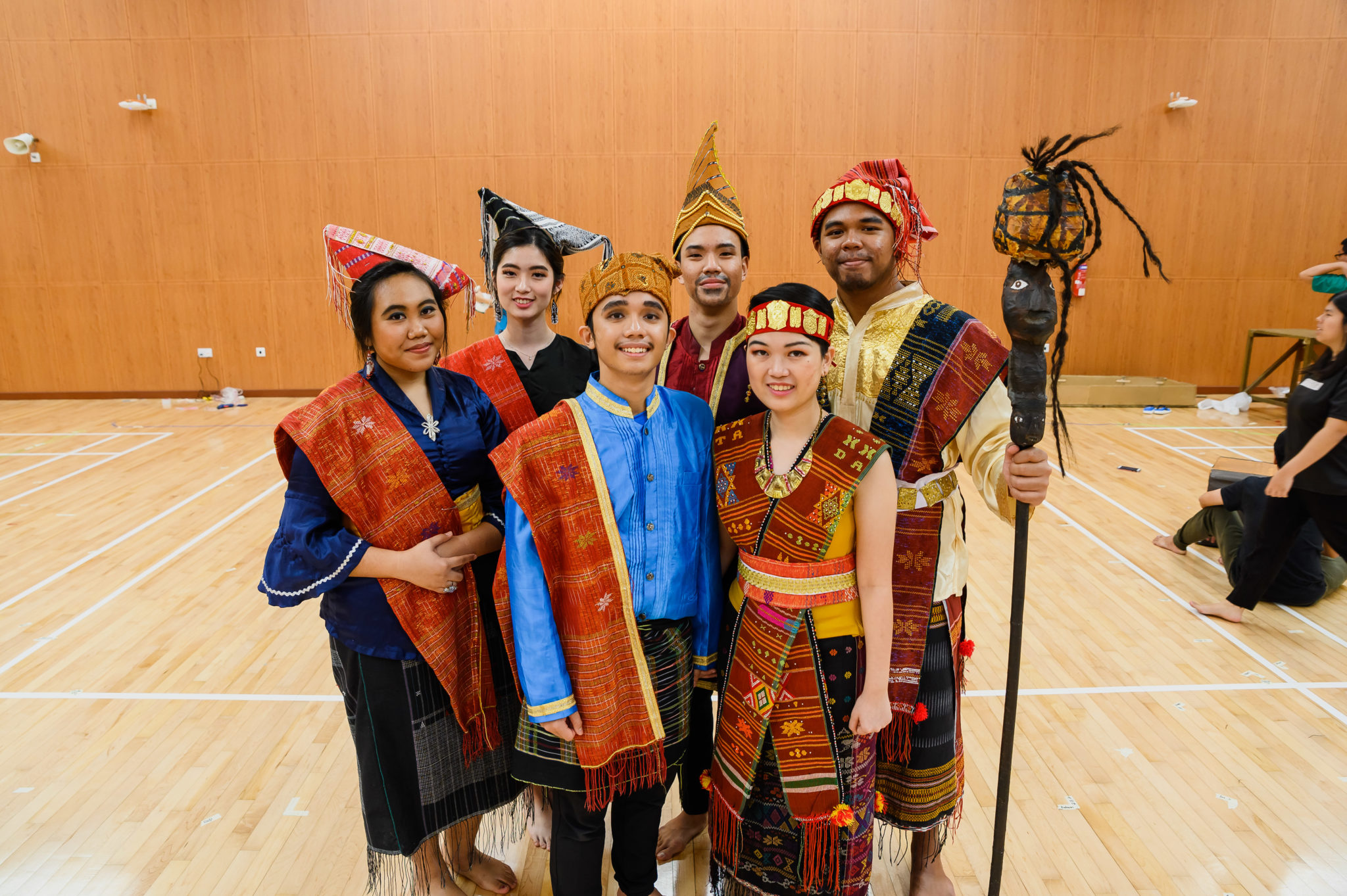 Cast members in traditional Batak costumes and headgear posing with a ceremonial staff