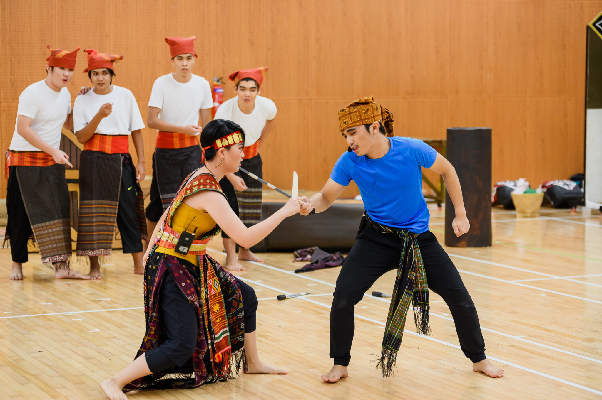 A cast member in traditional dress rehearsing a scene with an actor in a blue shirt