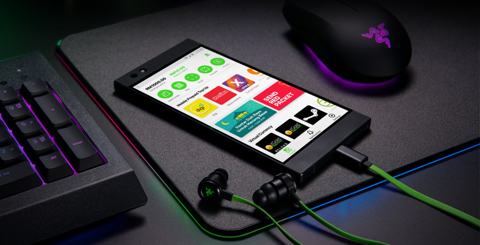 A Razer phone showing the Razer Pay app beside a keyboard and earphones