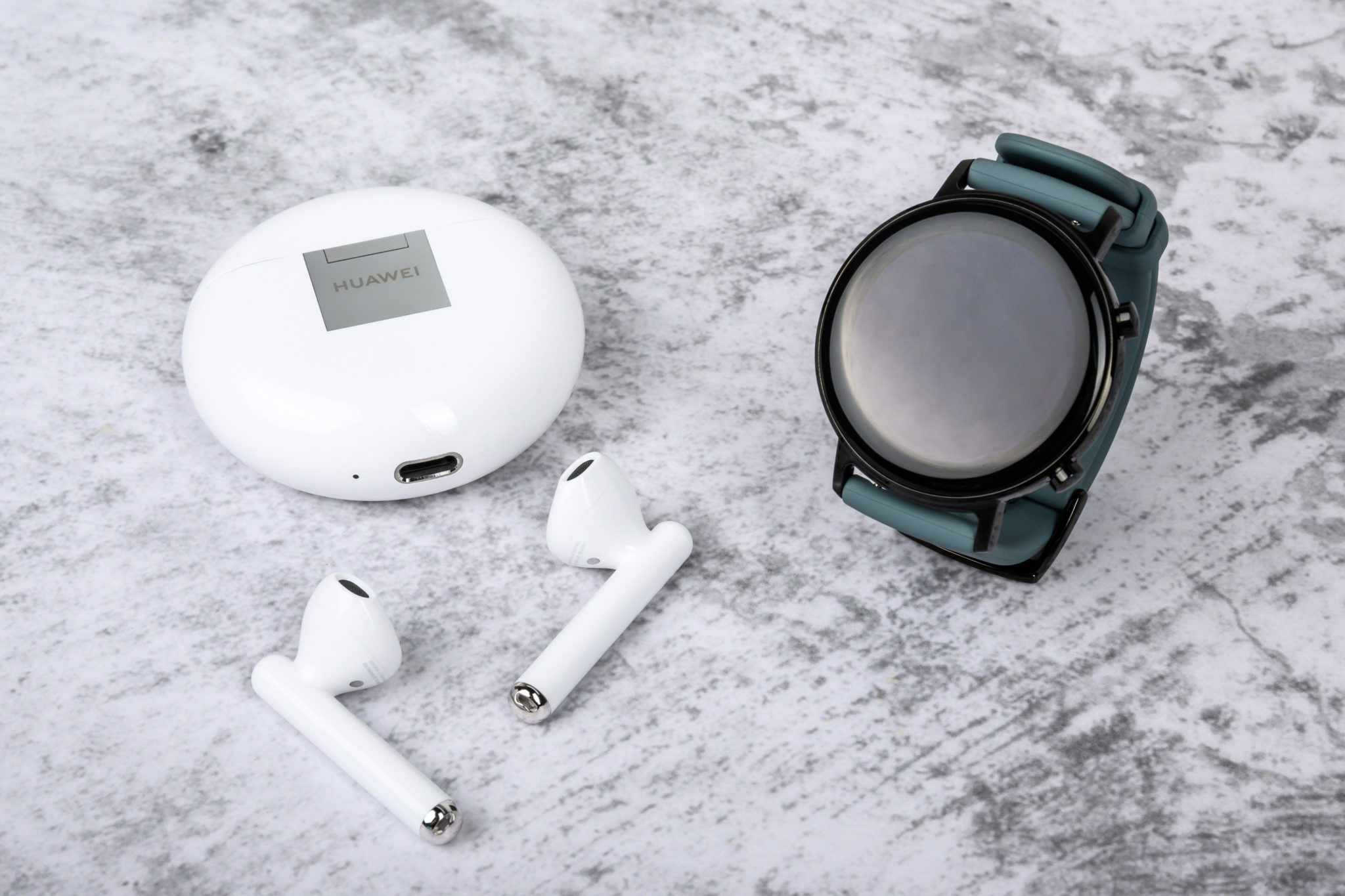 The Huawei Watch GT 2 beside a pair of white wireless earbuds and their case