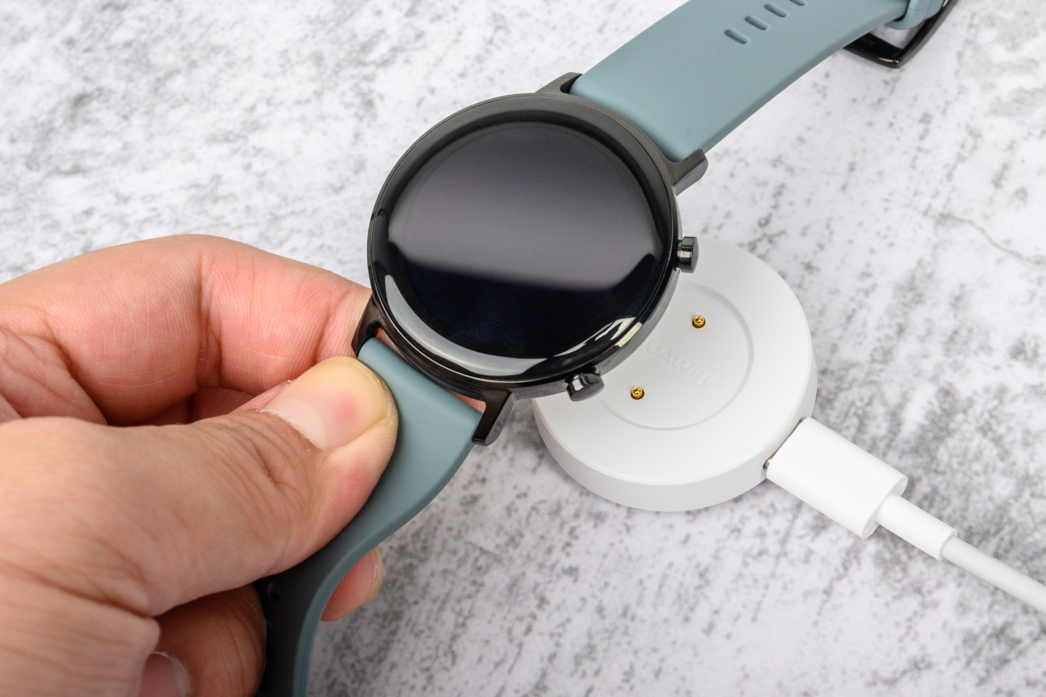 A hand placing the Huawei Watch GT 2 on its white charging dock
