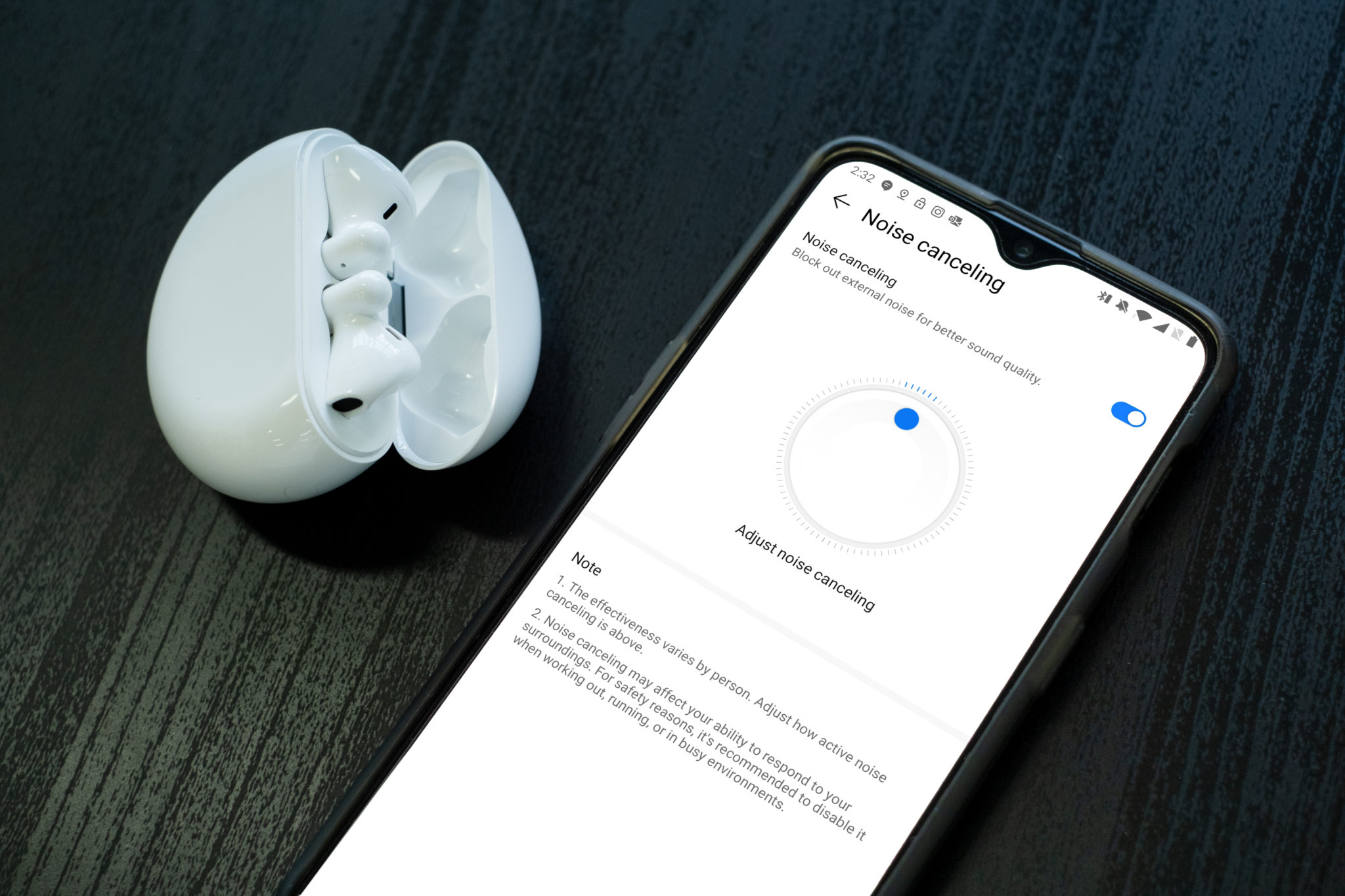 A phone showing the noise cancelling settings in the Huawei AI Life app beside the open charging case