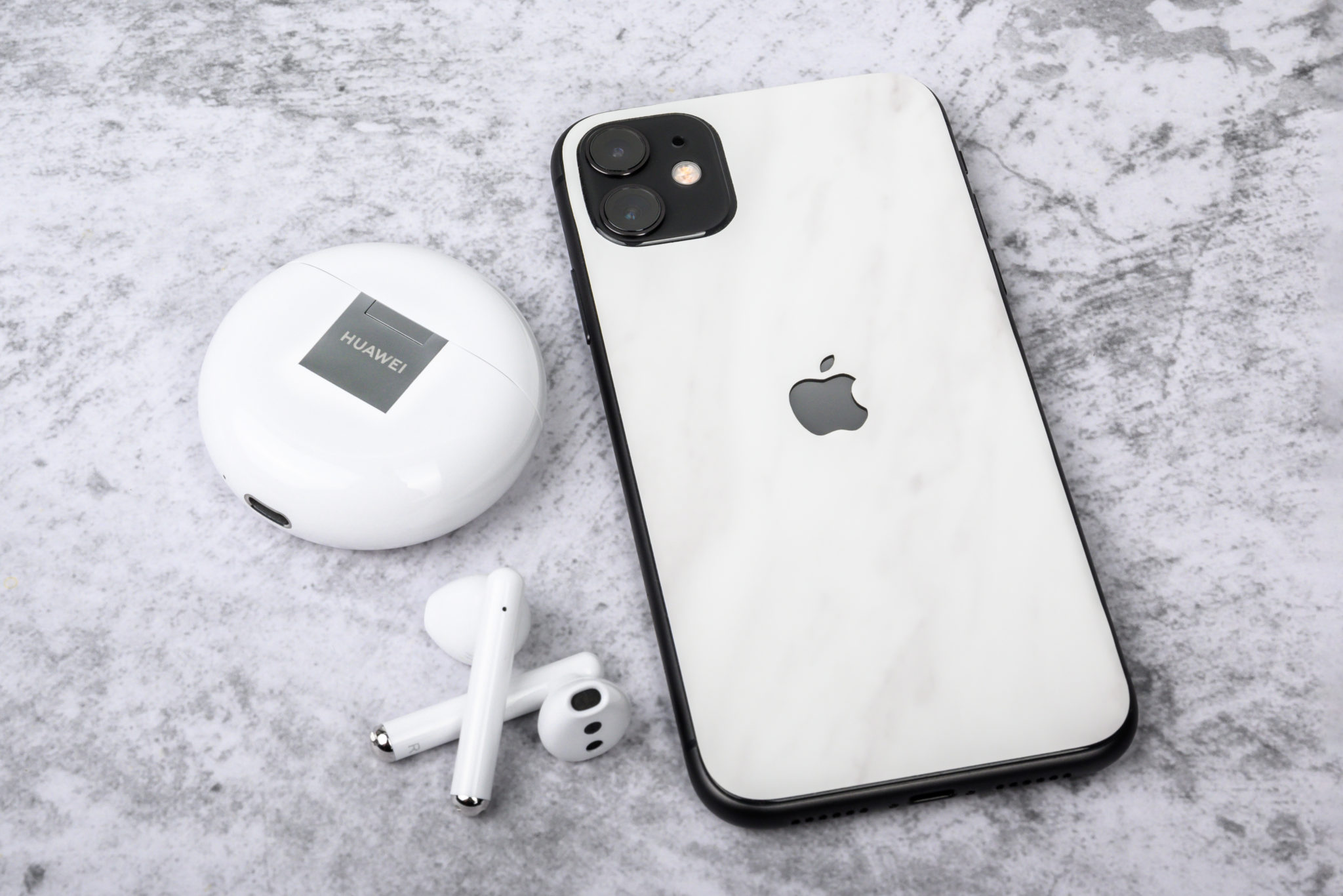 The Freebuds 3 and charging case beside a white iPhone on a marble surface
