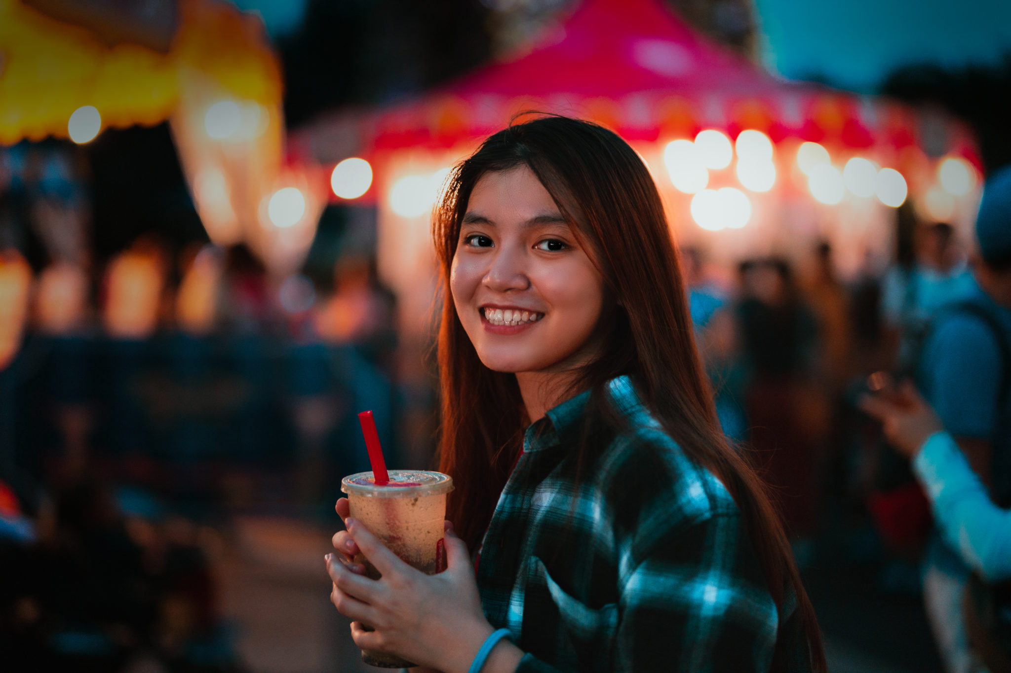 A smiling woman holding a drink at a night market, shot on the EOS RP
