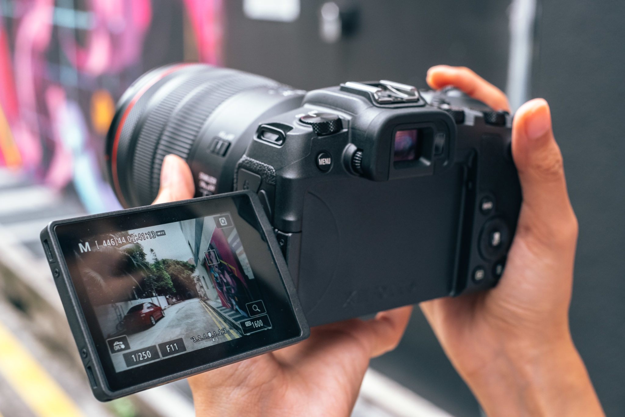 A hand holding the Canon EOS RP with its vari-angle screen turned out