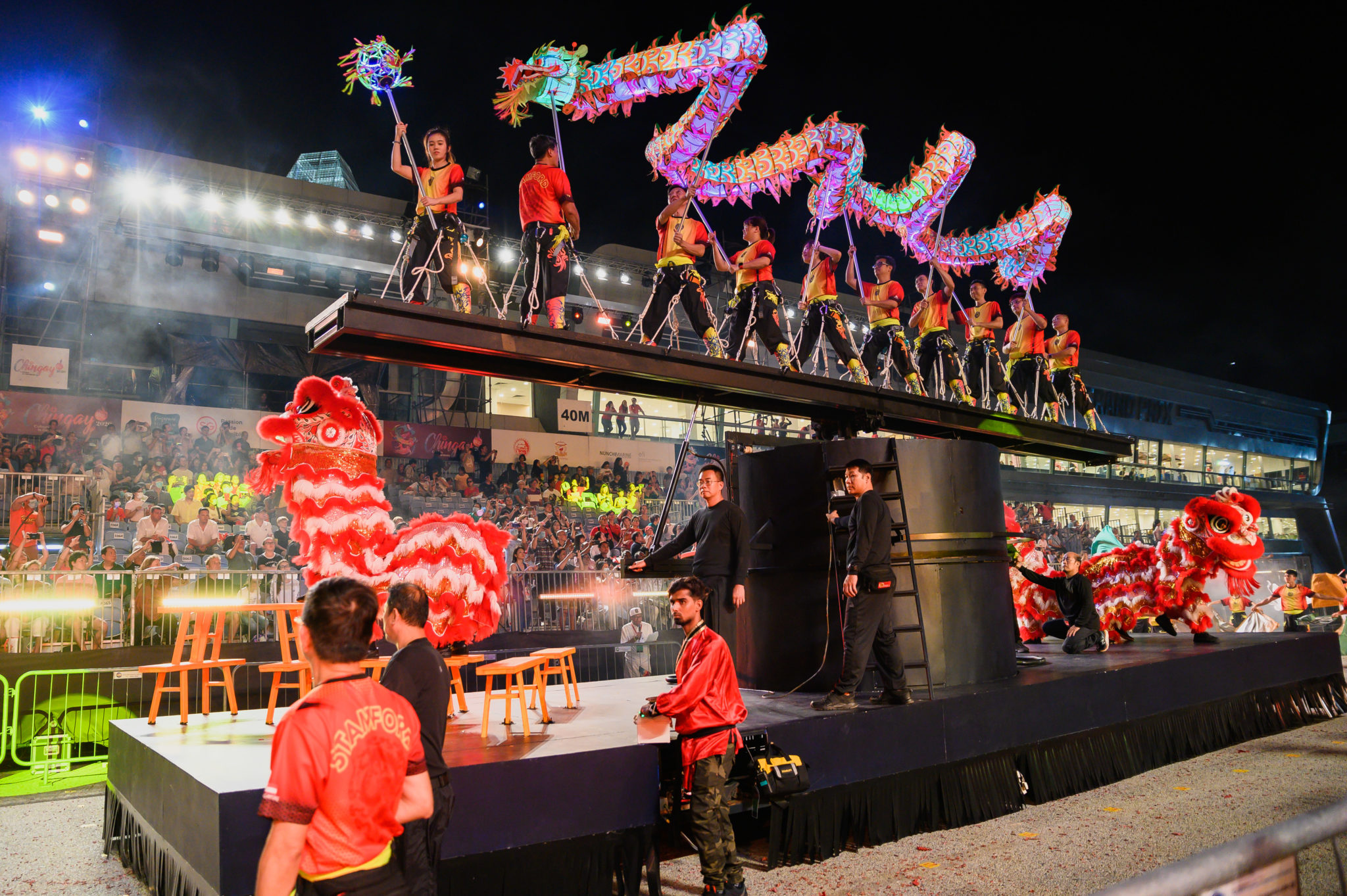 Performers on a stage lifting a long glowing dragon above a crowd at Chingay