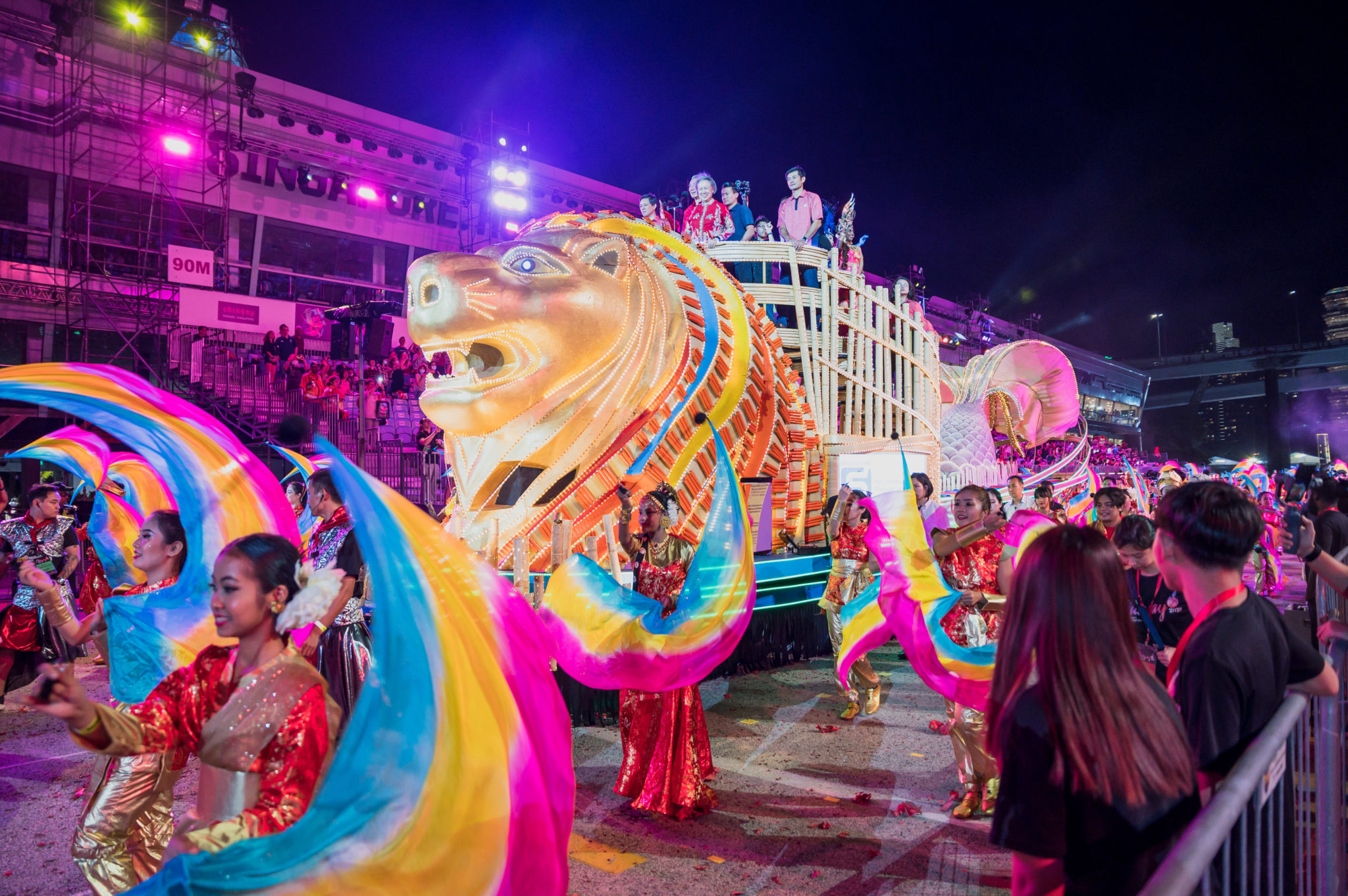 A colourful lion-headed float at night with dancers in red and gold costumes at Chingay