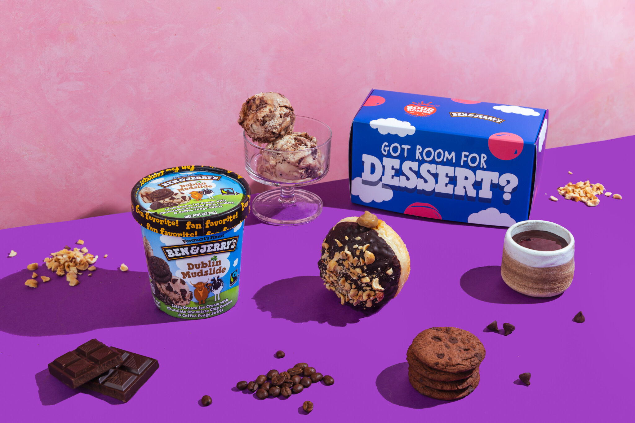 A Ben & Jerry's pint with a Dublin' Down doughnut, chocolate and cookies on a purple backdrop