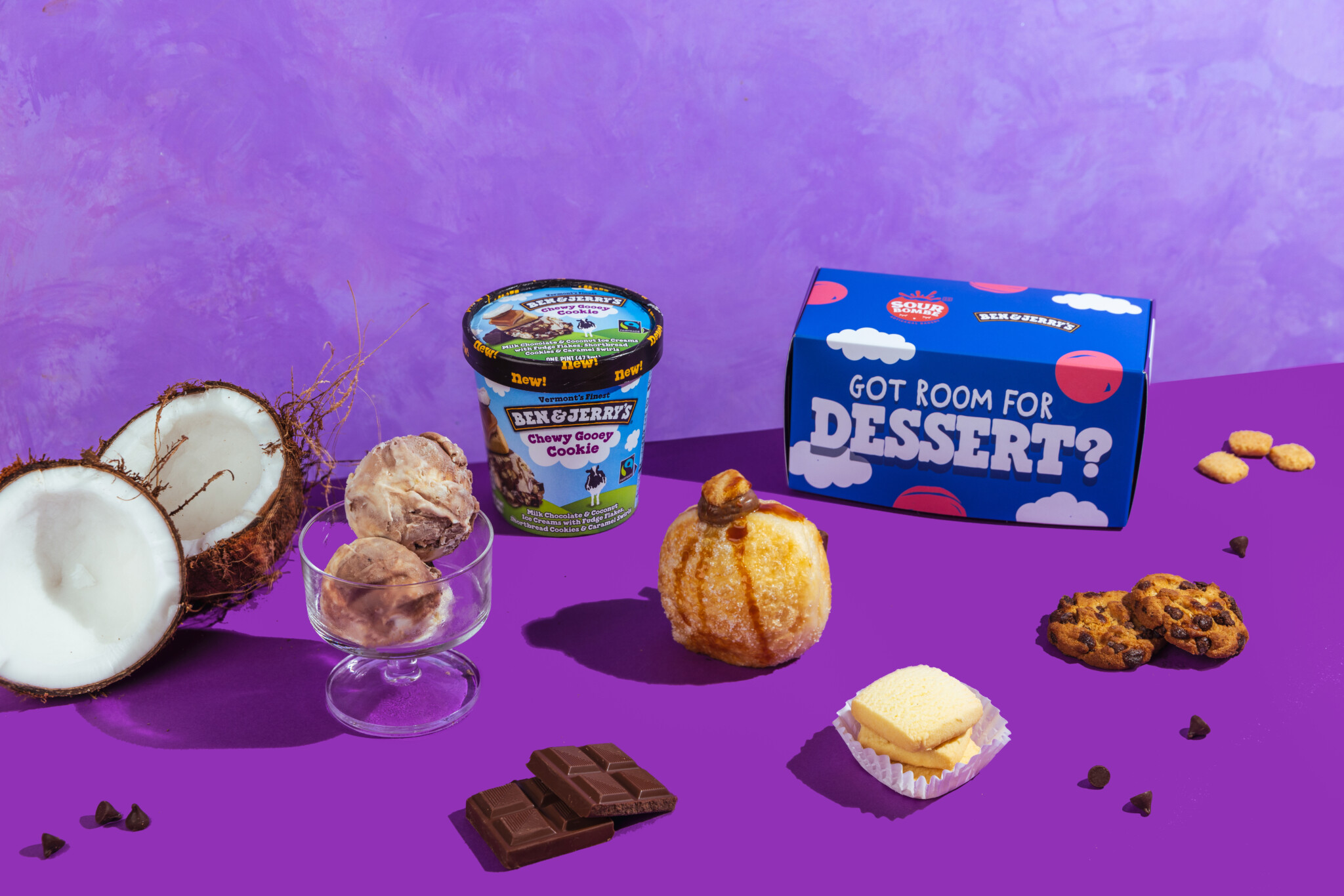 A Ben & Jerry's pint beside a Gooey Glory doughnut, cookies and ice cream cups on a purple backdrop