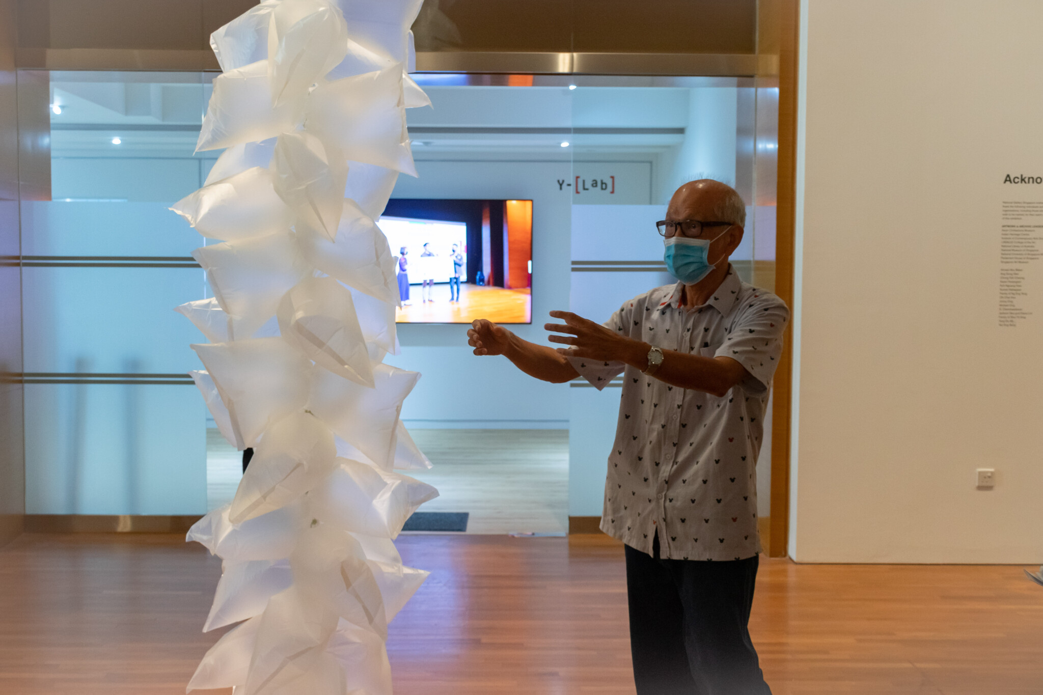 Lim Leong Seng gesturing beside New Era, a tall column of air-filled plastic bags in the gallery