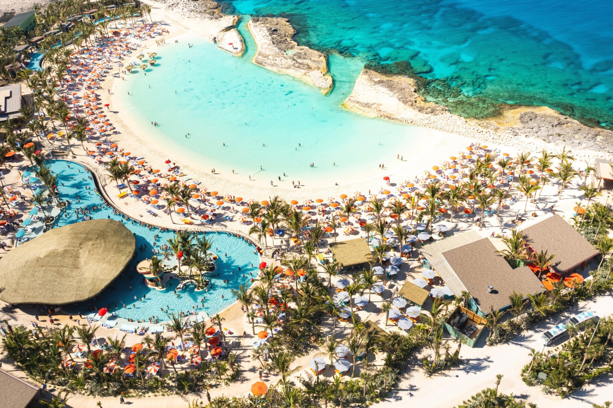 An aerial view shows a large pool, palm trees and rows of umbrellas at CocoCay.
