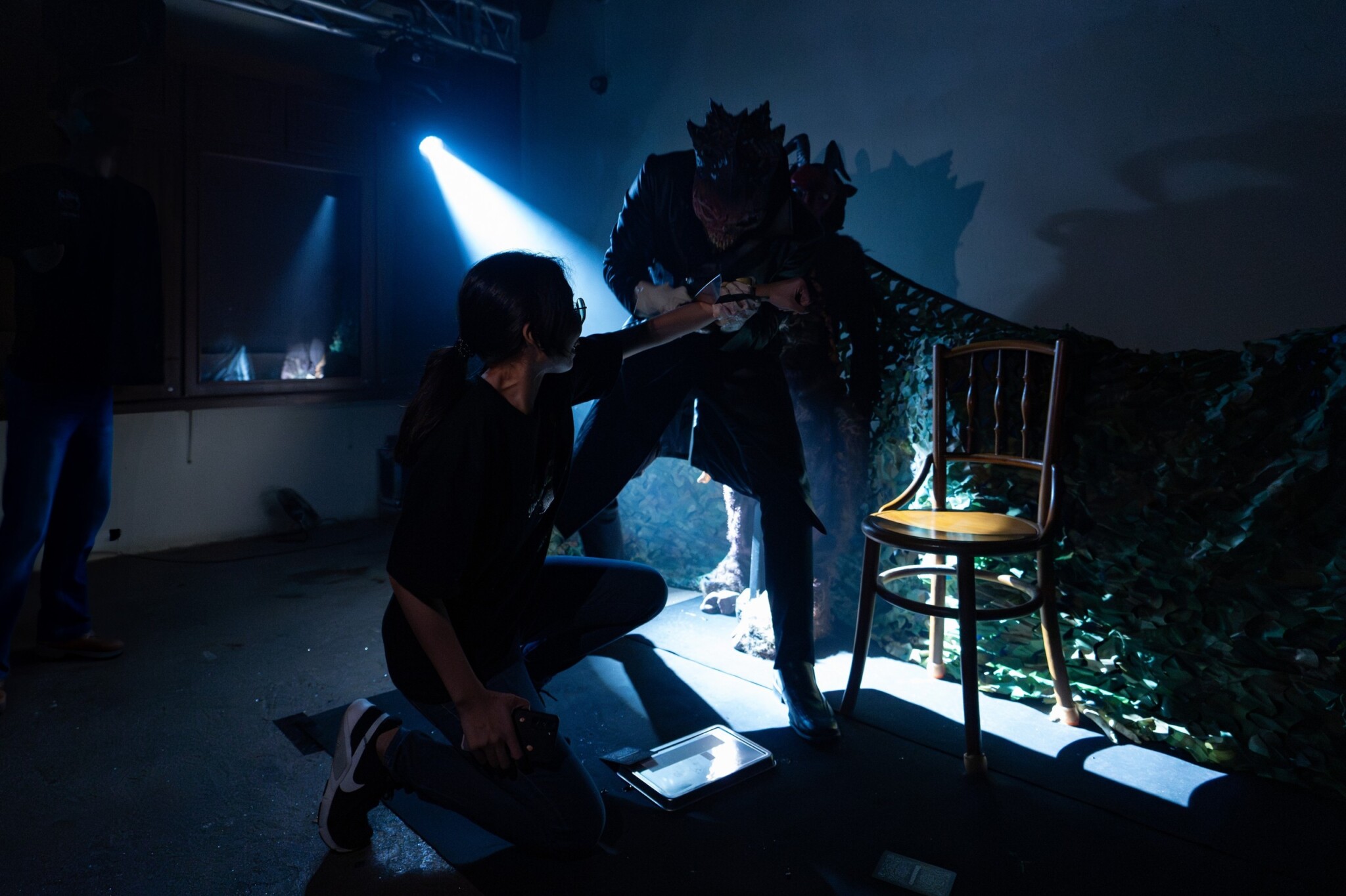 A seated visitor faces a costumed horror performer in a dim room.