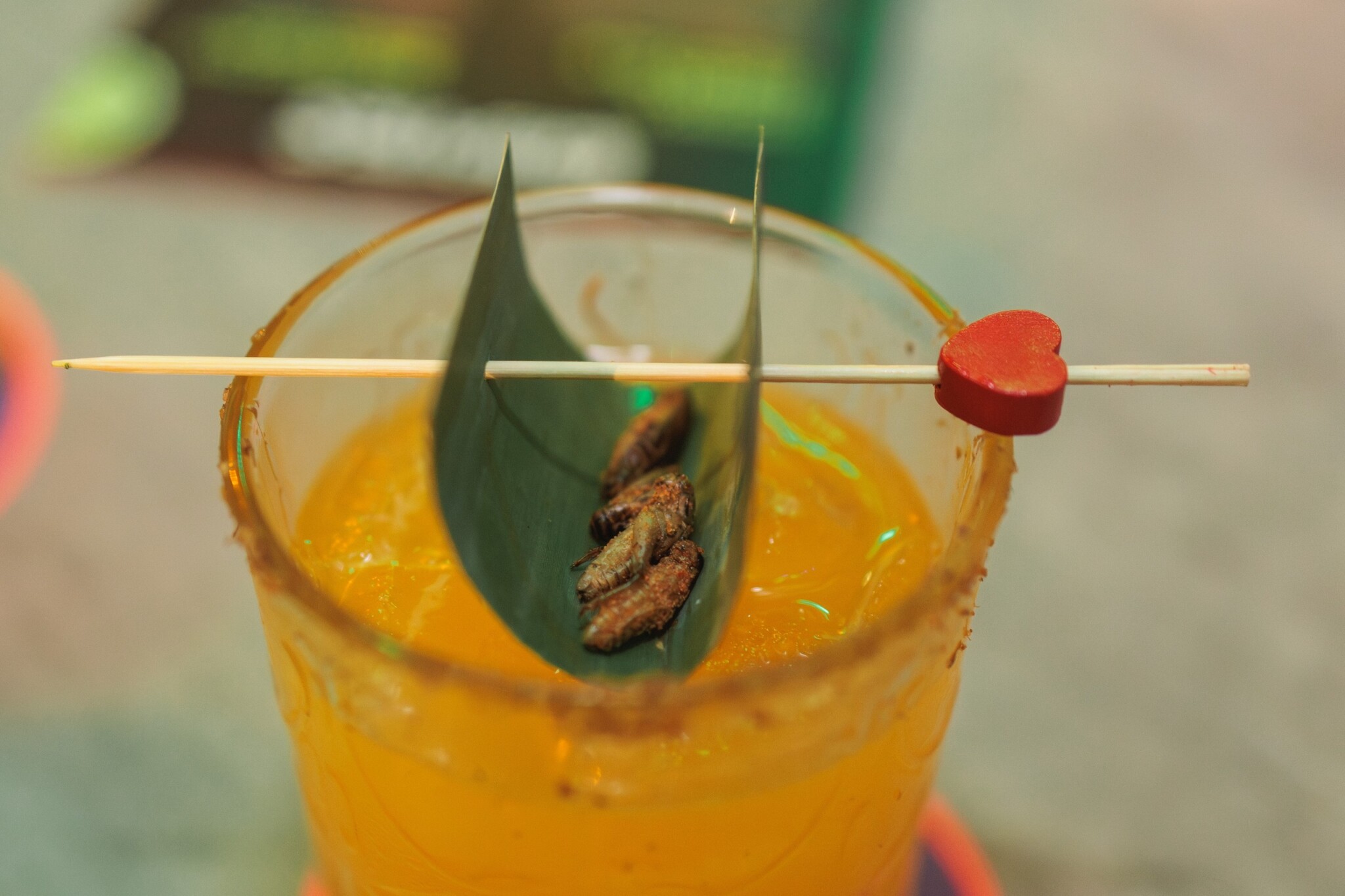 An orange cocktail is topped with a leaf holding cricket garnishes.