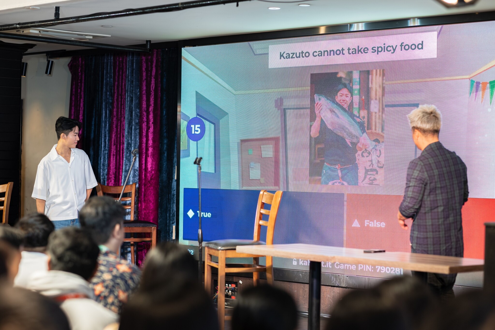 Kazuto and the host stand beside a projected quiz question during the fan meet.