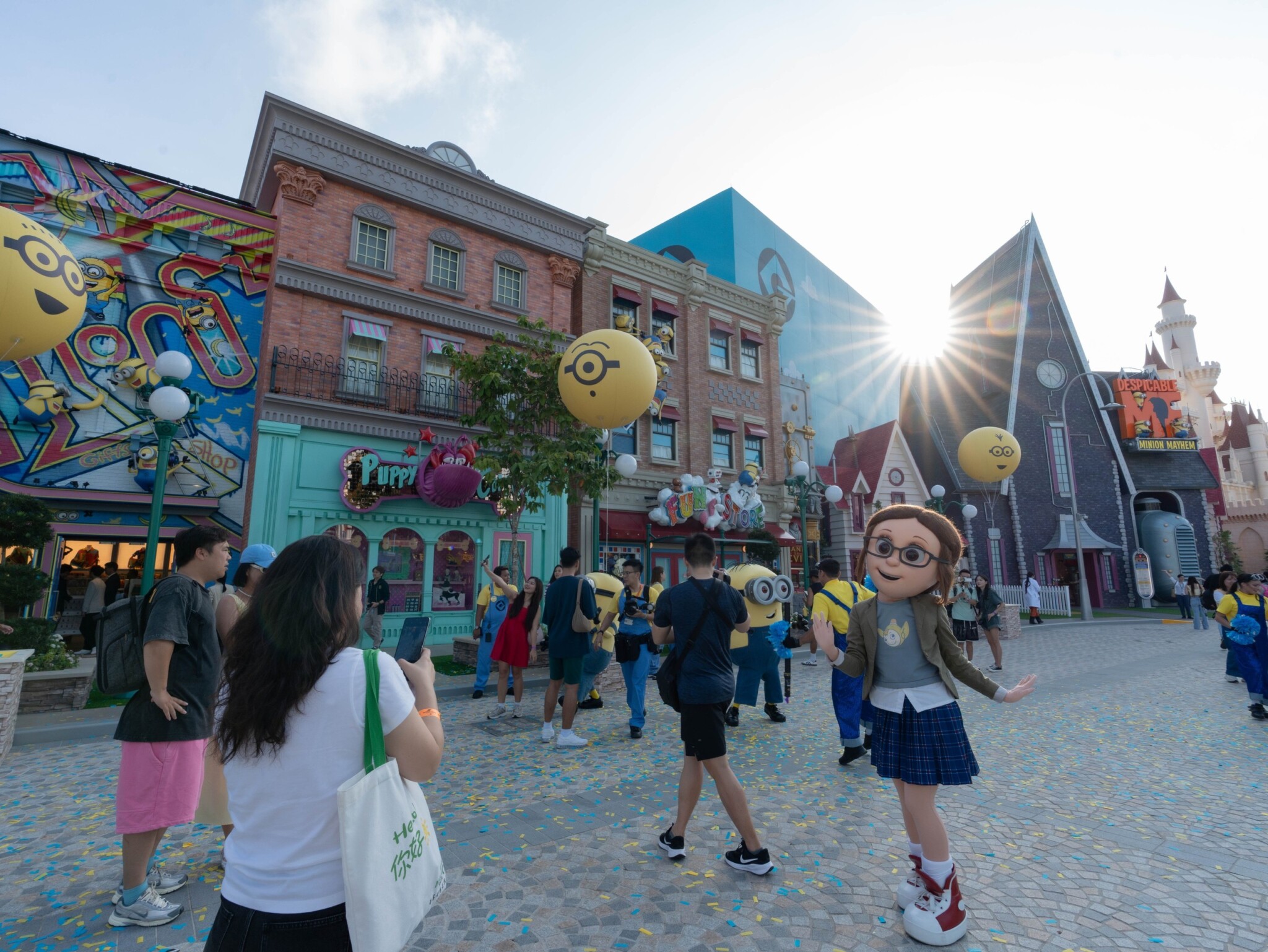 Visitors walk along a sunny street lined with colourful Minion Land buildings.