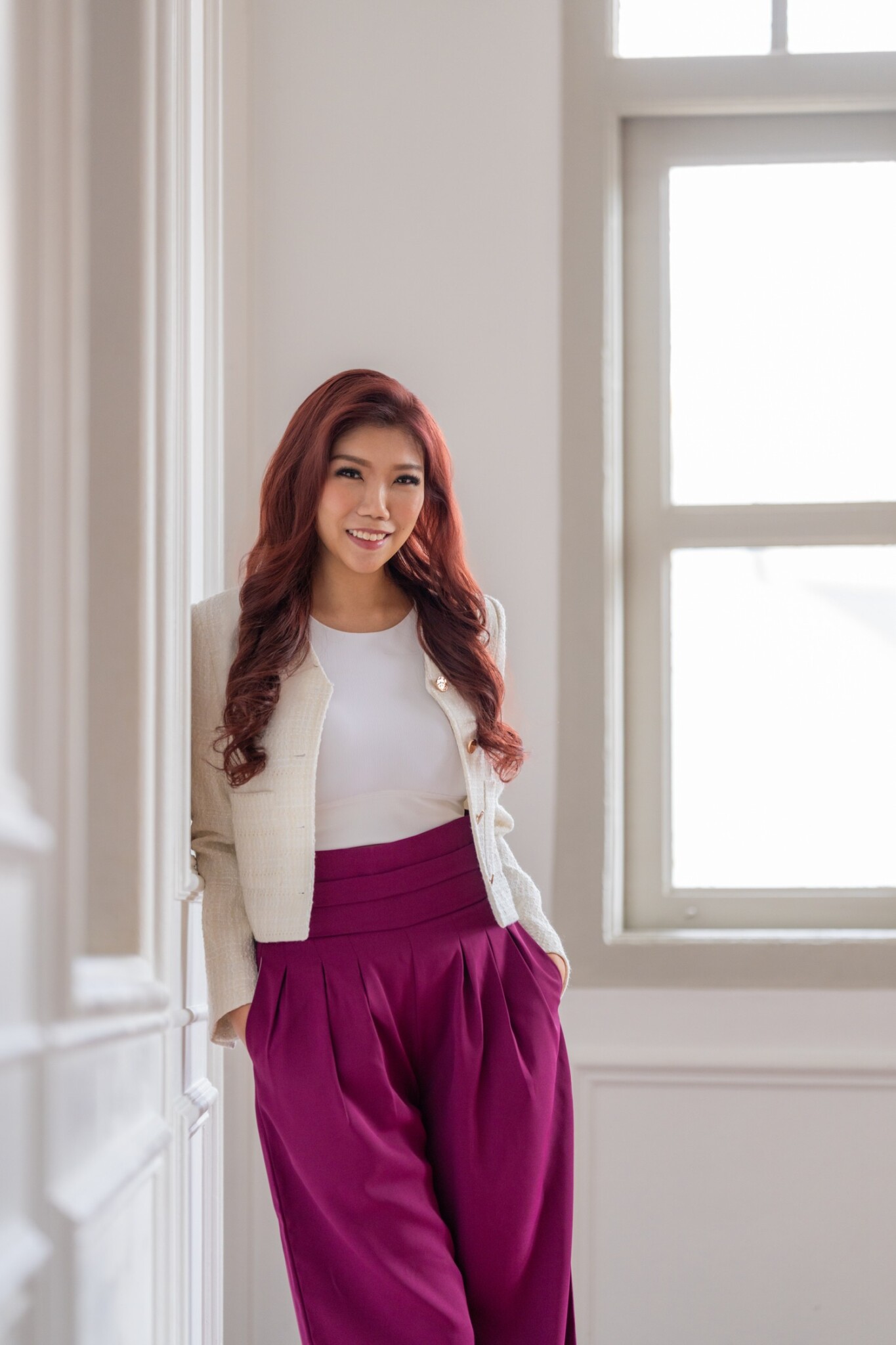 Michelle Ngiam stands by a window wearing a white cardigan and purple trousers.