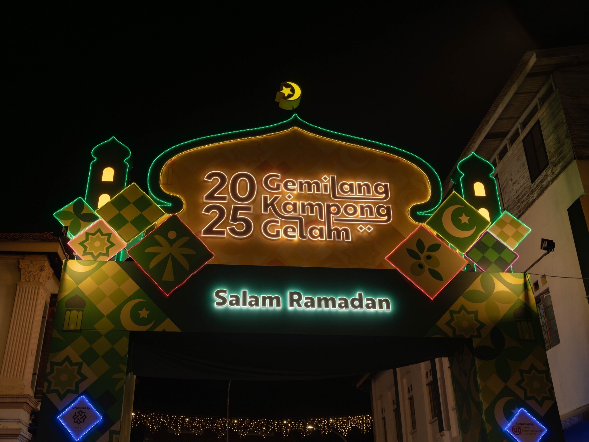 Visitors walk beneath the illuminated Gemilang Kampong Gelam bazaar entrance.