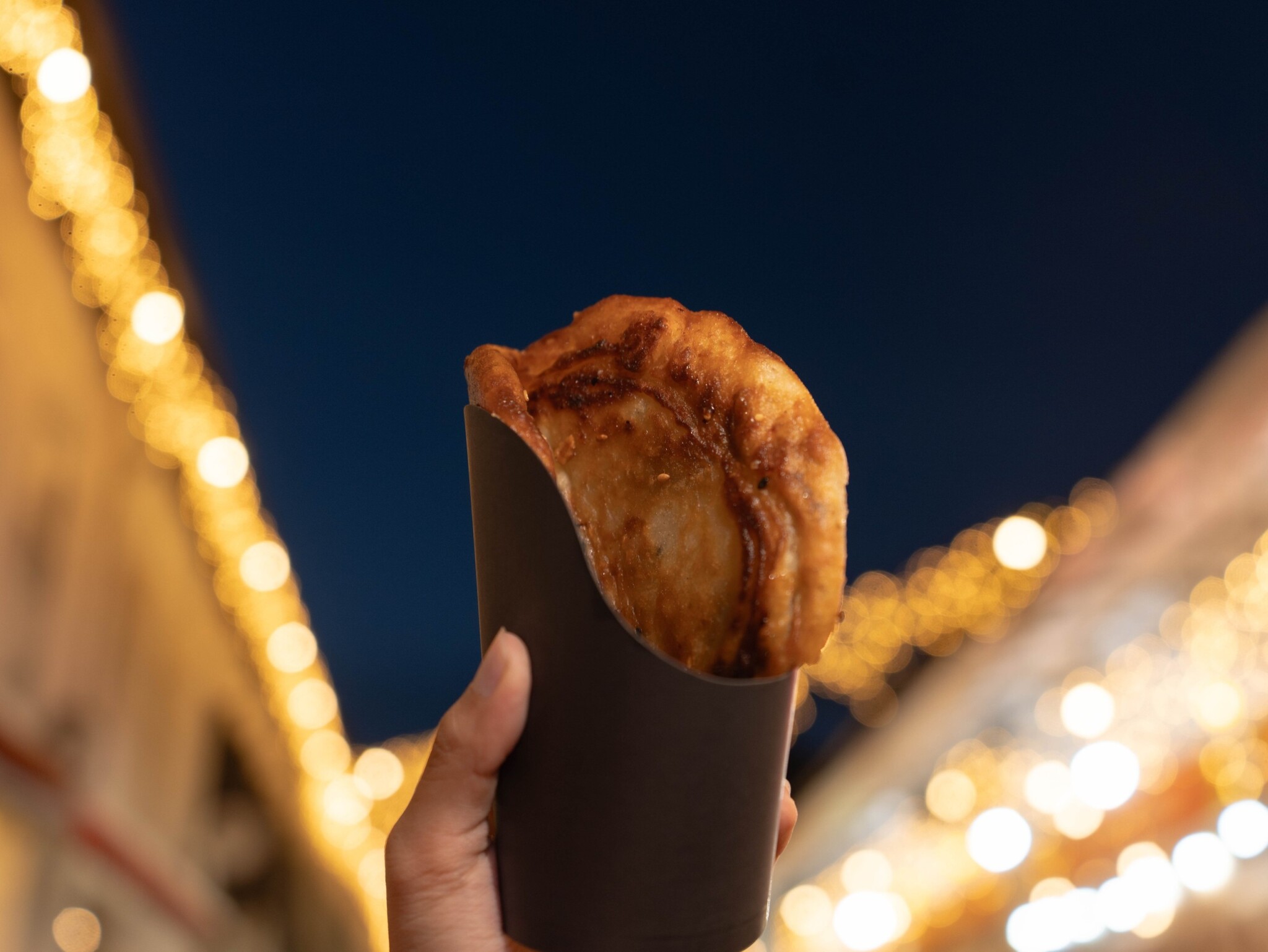 A hand holds a golden pancake in a paper sleeve at the bazaar.