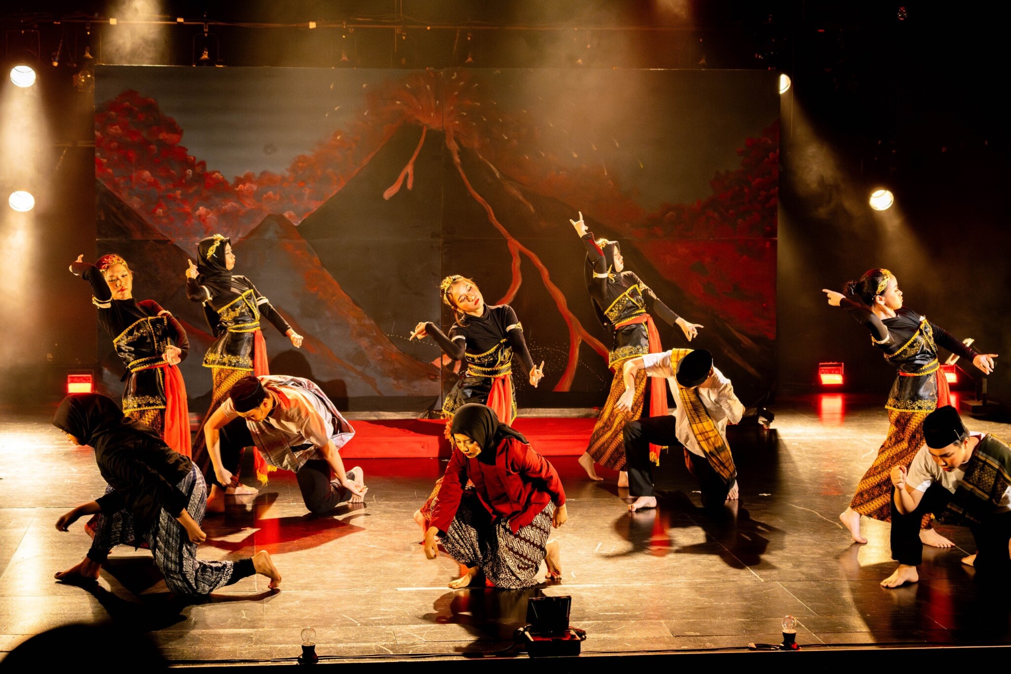 Dancers in orange and black costumes perform on stage.