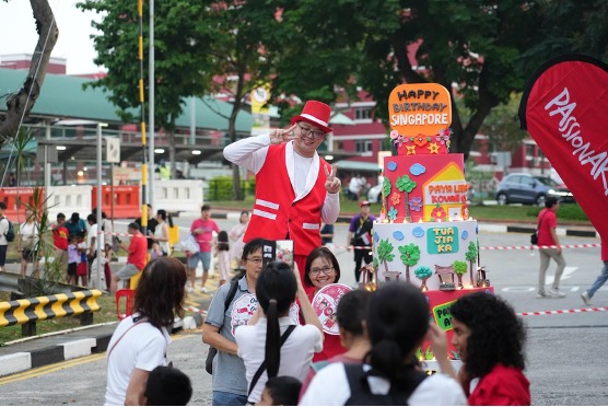 A man on a raised platform beside the multi-tiered Happy Birthday Singapore display, with a crowd gathered around