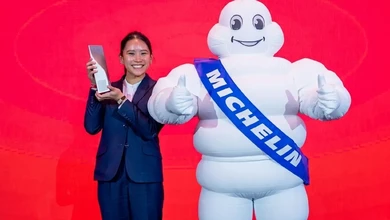Maryjoy Lim holding a glass Michelin Service Award trophy beside the Michelin Man mascot