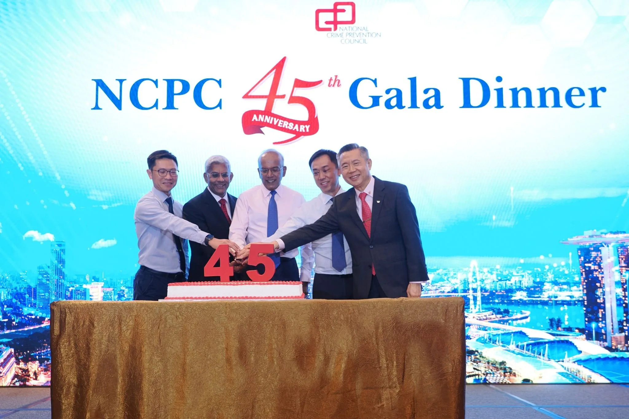Five men in business attire cut a cake marked 45 on stage at the NCPC 45th Anniversary Gala Dinner