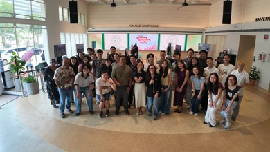A large group poses for a photo in the lobby of Temasek Shophouse beneath screens for the TF-NUS Heritage Champions Showcase