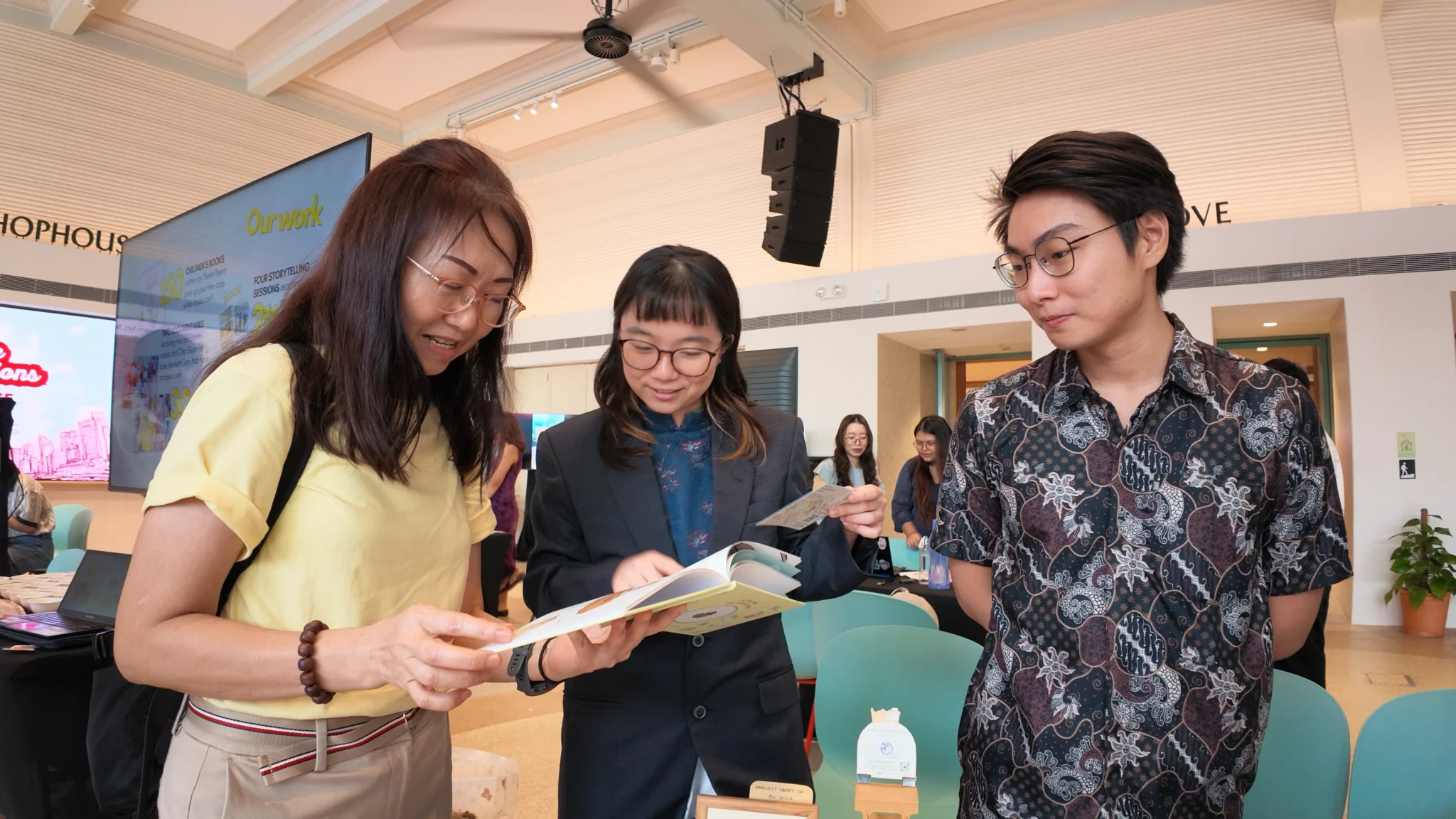 Three attendees look at an open illustrated children's book at a project stand