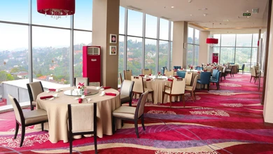 Elevated hotel restaurant dining room with round tables and floor-to-ceiling windows overlooking a hillside town