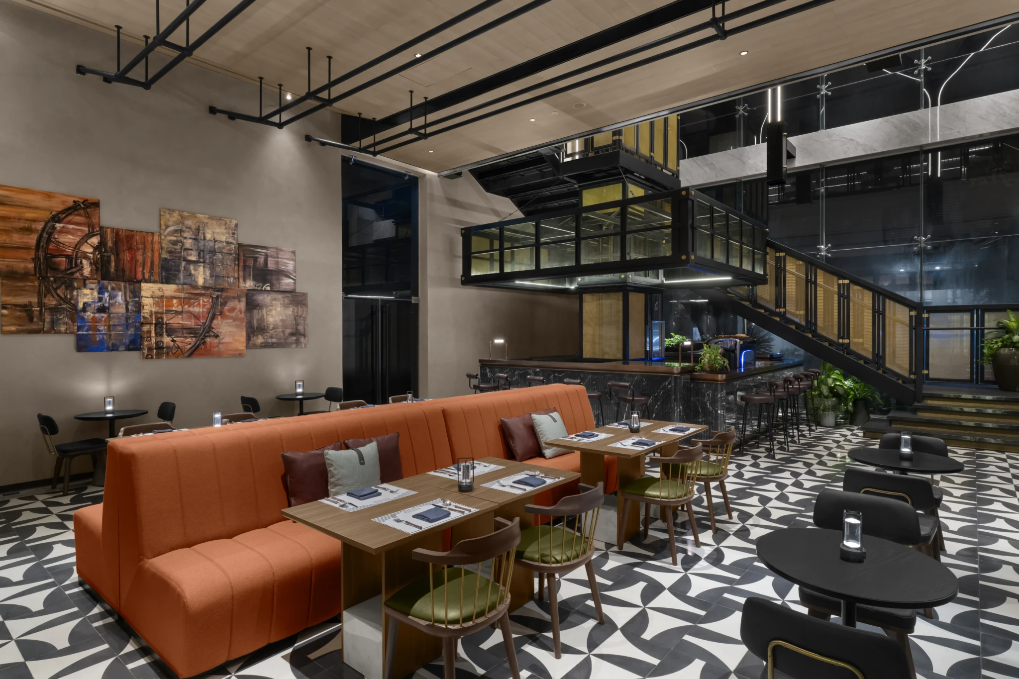 Modern hotel lounge with an orange banquette booth, patterned floor tiles, and a marble-topped bar