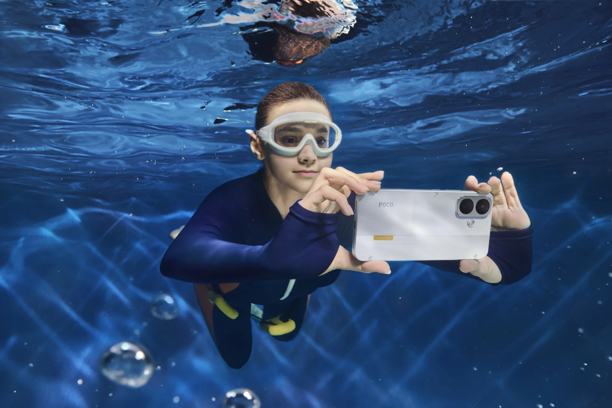 Swimmer in a wetsuit photographing with a POCO X8 underwater
