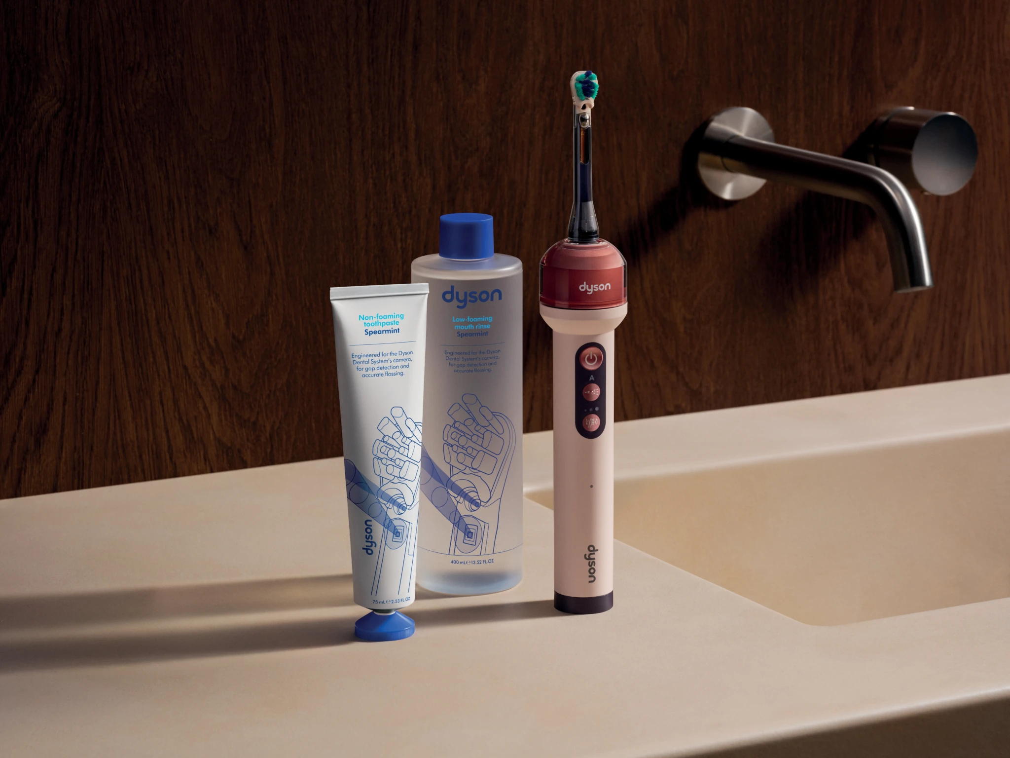 Dyson CameraJet toothbrush standing beside matching spearmint mouthrinse bottles at a bathroom basin