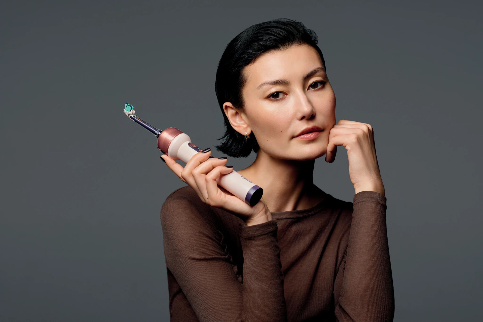 A woman holding the Dyson CameraJet toothbrush with its camera visible in the brush head